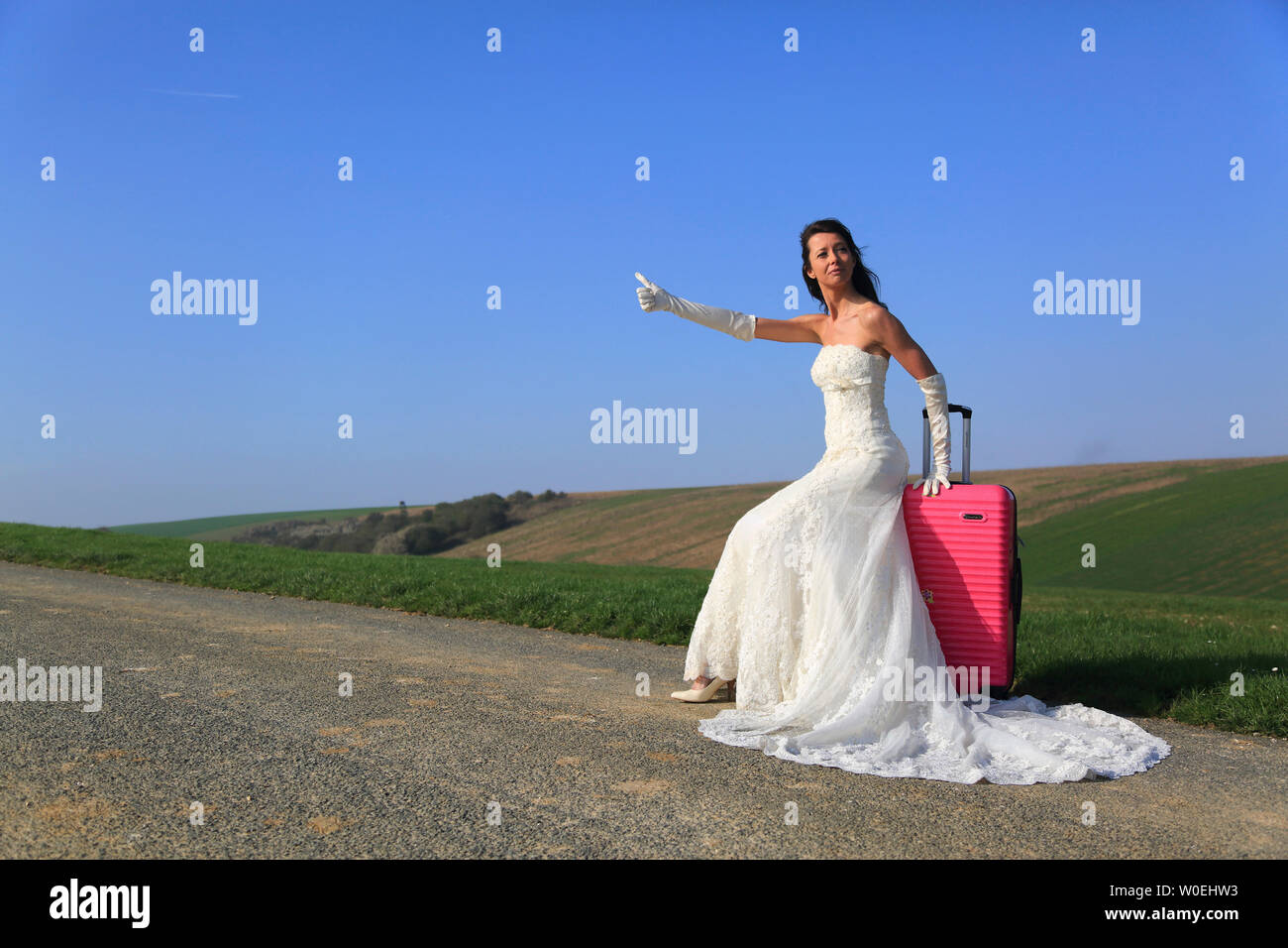 Bride hitchhiking with pink suitcase Stock Photo