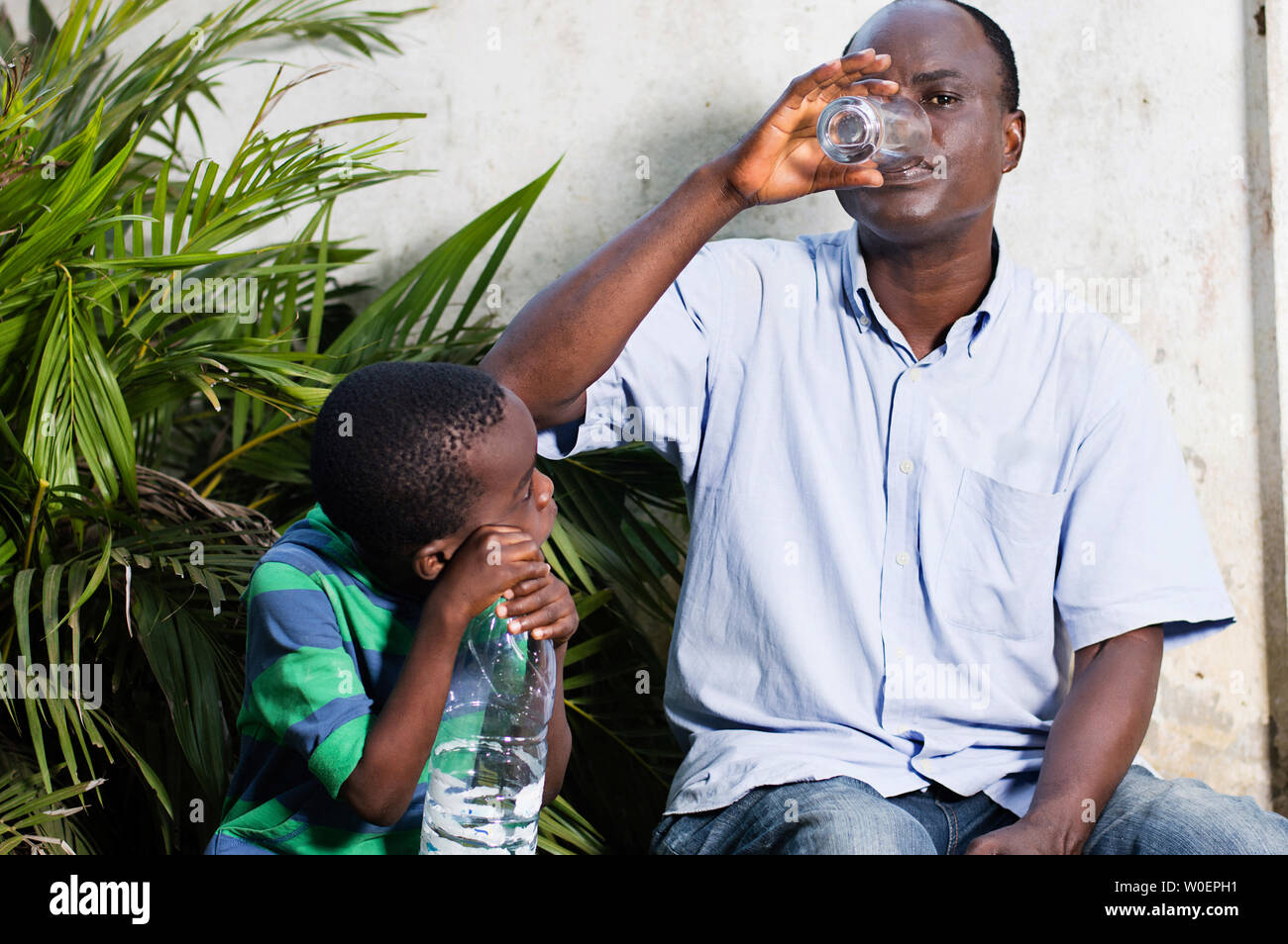 middle-aged man drinks water in a glass and child watching. Stock Photo