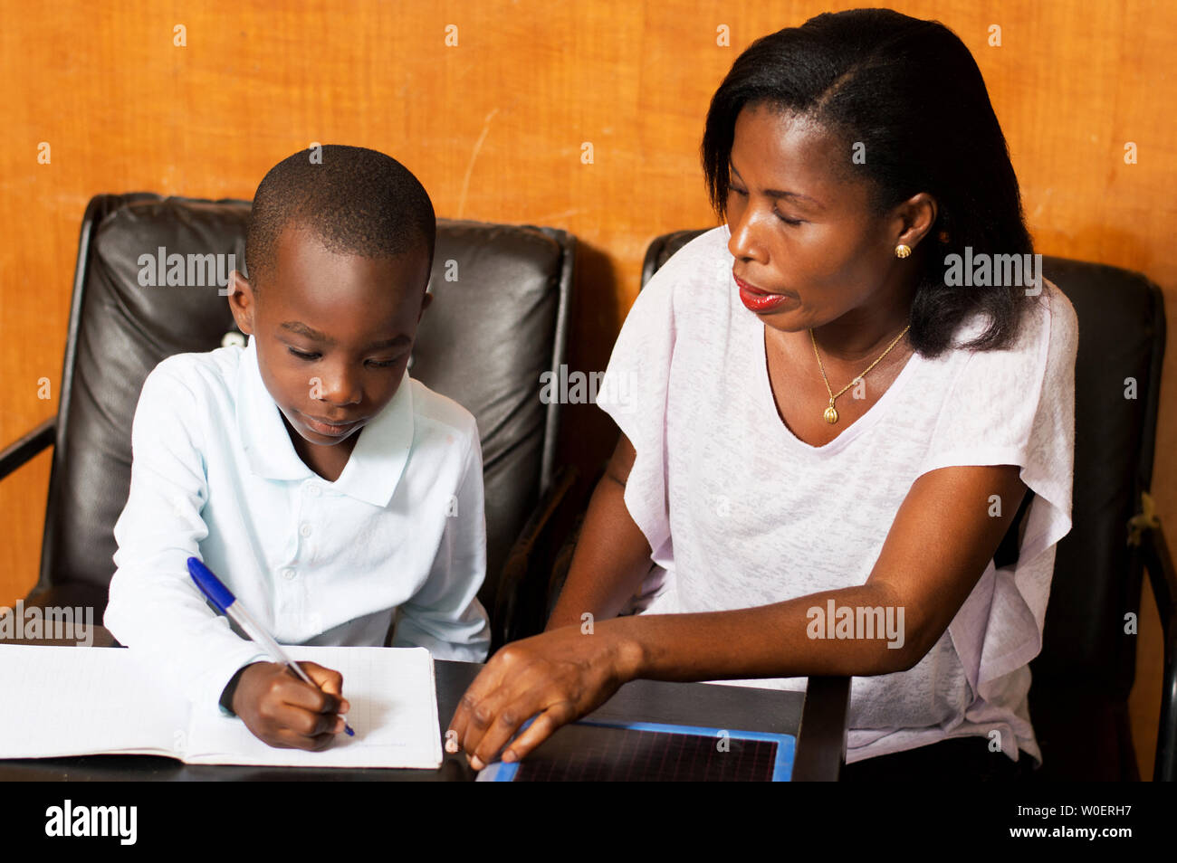 Mom attends child writing in his notebook. Stock Photo