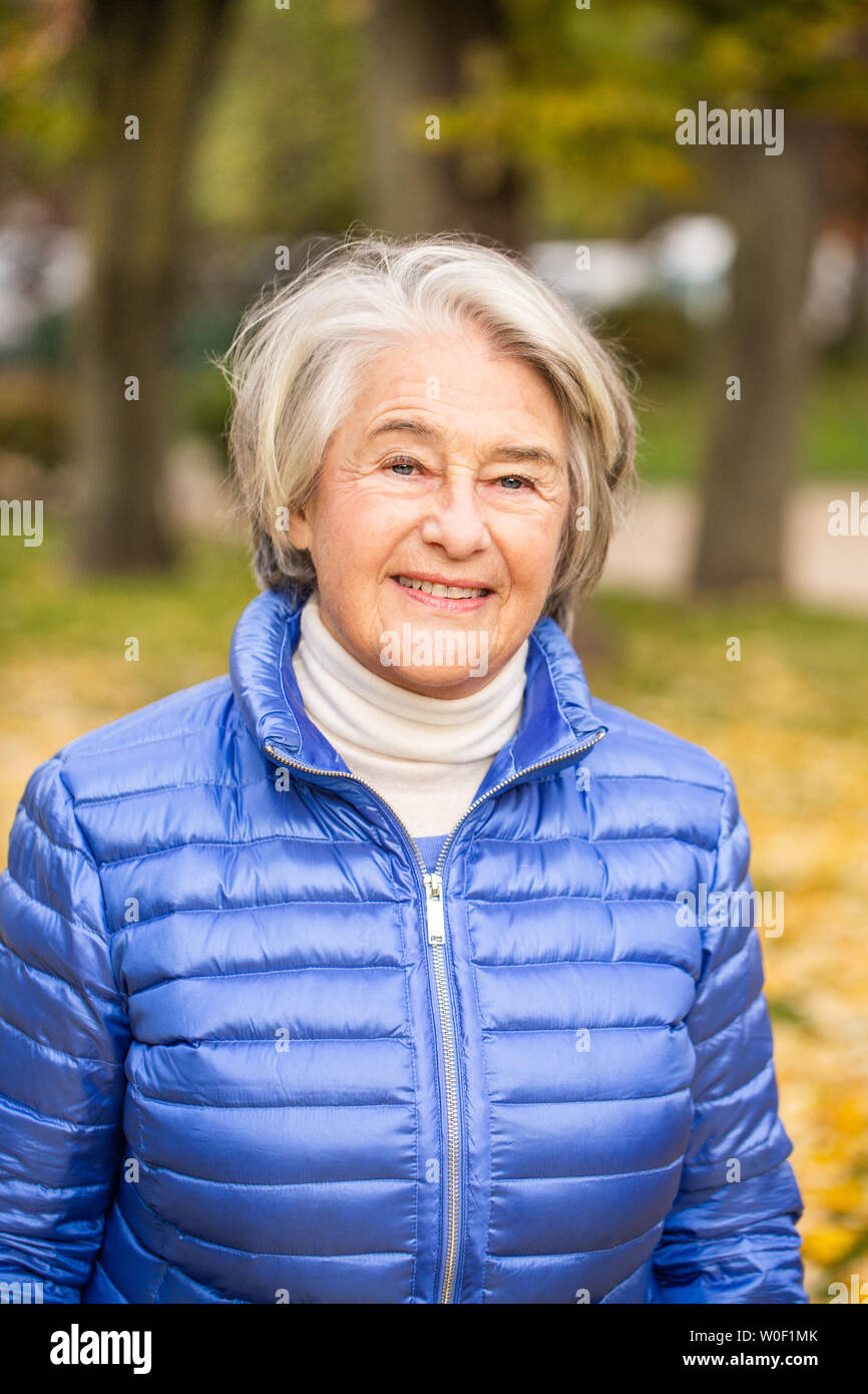 Portrait of a smilling pretty senior woman in a parc front yellow leaves. Stock Photo