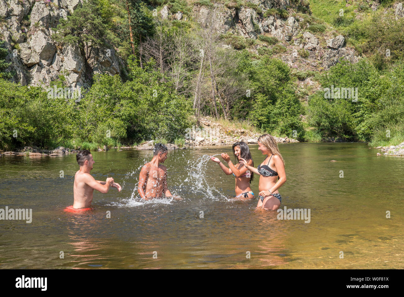 Auvergne - Rhone-Alpes - Haute-Loire - Bathing in the Loire at Arlemdes under the basalt cliffs. Four friends, two boys and two girls, are splattering each other in the river. Stock Photo