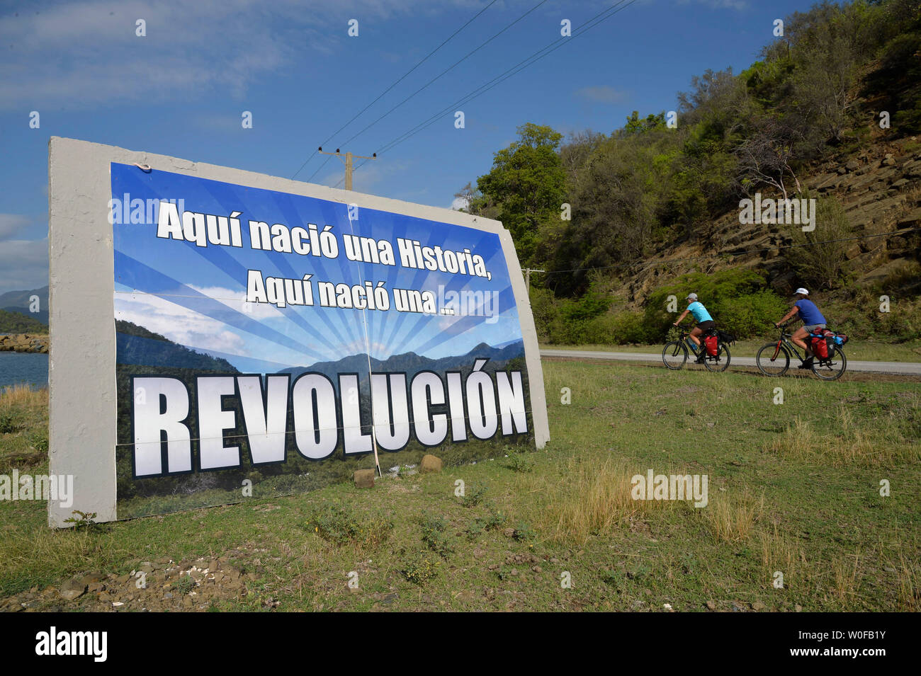 Cuba, 2 cyclists are riding in front of a huge sign doing the propaganda of  the cuban revolution Stock Photo