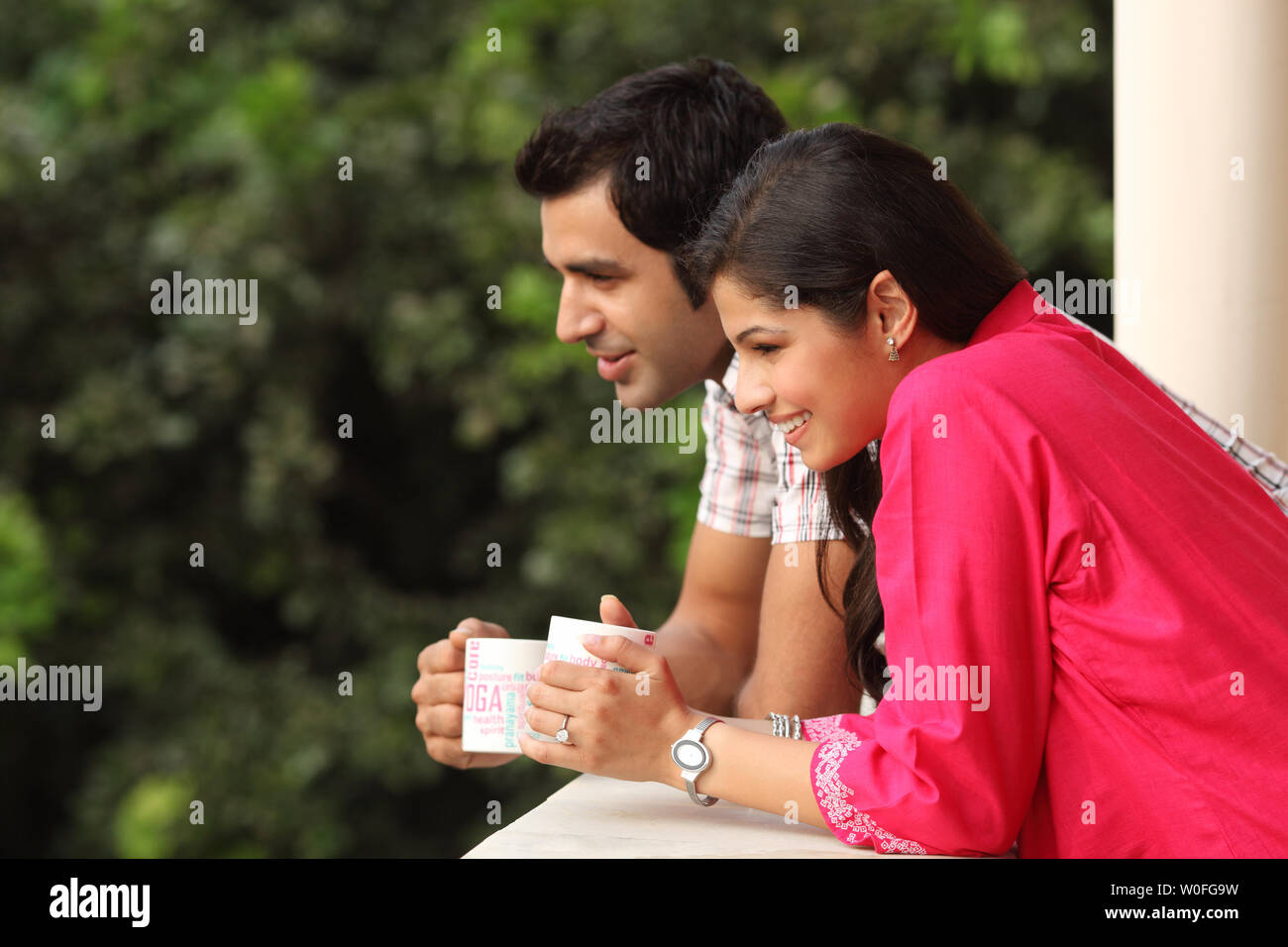 Indian couple leaning against a railing and drinking coffee Stock Photo