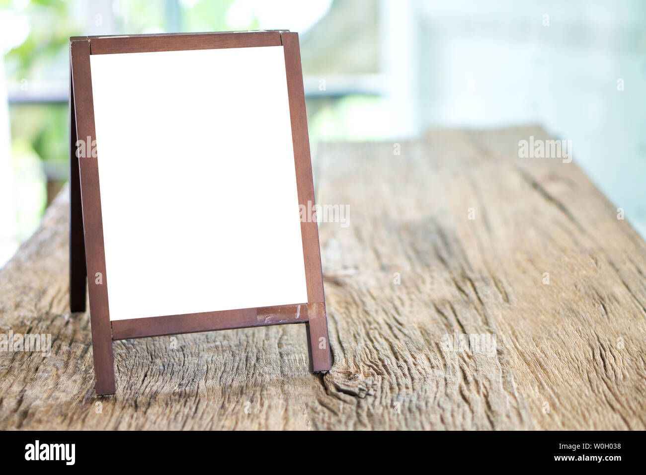 Mock up blank advertising whiteboard with easel standing on wood table in cafe and bar restaurant for display or montage of design space for text. Stock Photo