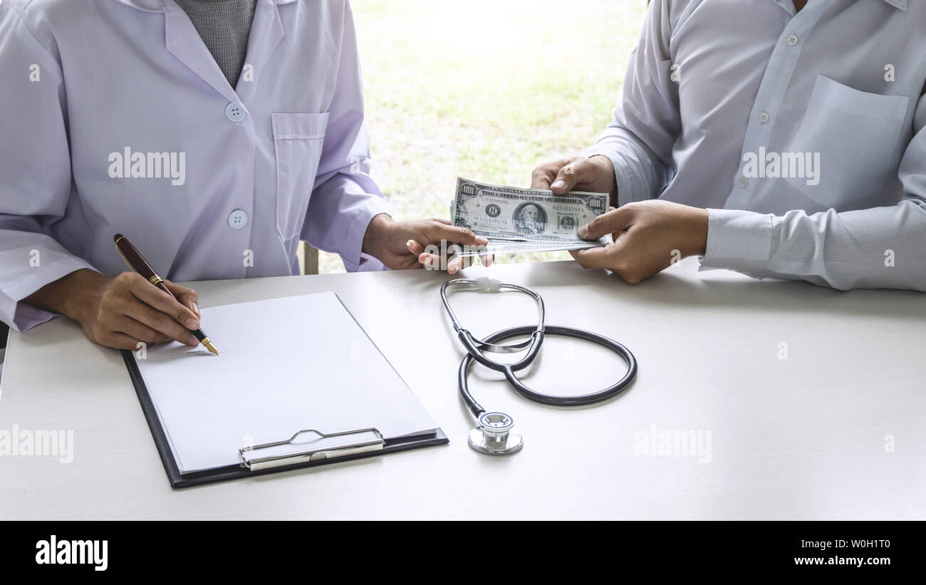 Patient giving bribe money the form of dollar bills to Female doctor while give success the deal to contract agreement, Bribery and corruption concept Stock Photo
