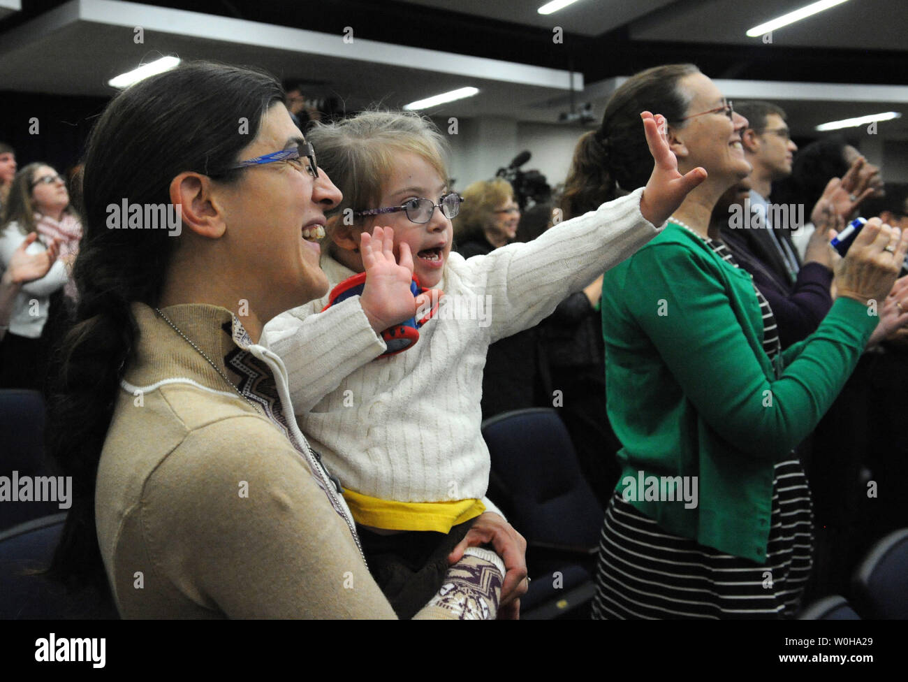 Hope Katz-Zogby, age 3, applauds with her mother Elizabeth as they listen to U.S. President Barack Obama discuss the successes of the Affordable Care Act in the Eisenhower Executive Office Building in Washington, DC on December 3, 2013.   Hope, from Baltimore, Maryland, has Down Syndrome but is guaranteed health insurance under the ACA, since insurance companies cannot bar anyone with pre-existing medical conditions. Obama promised that his signature healthcare law was going to remain as long as he was president and that the troubled www.healthcare.gov website was working well for the vast maj Stock Photo