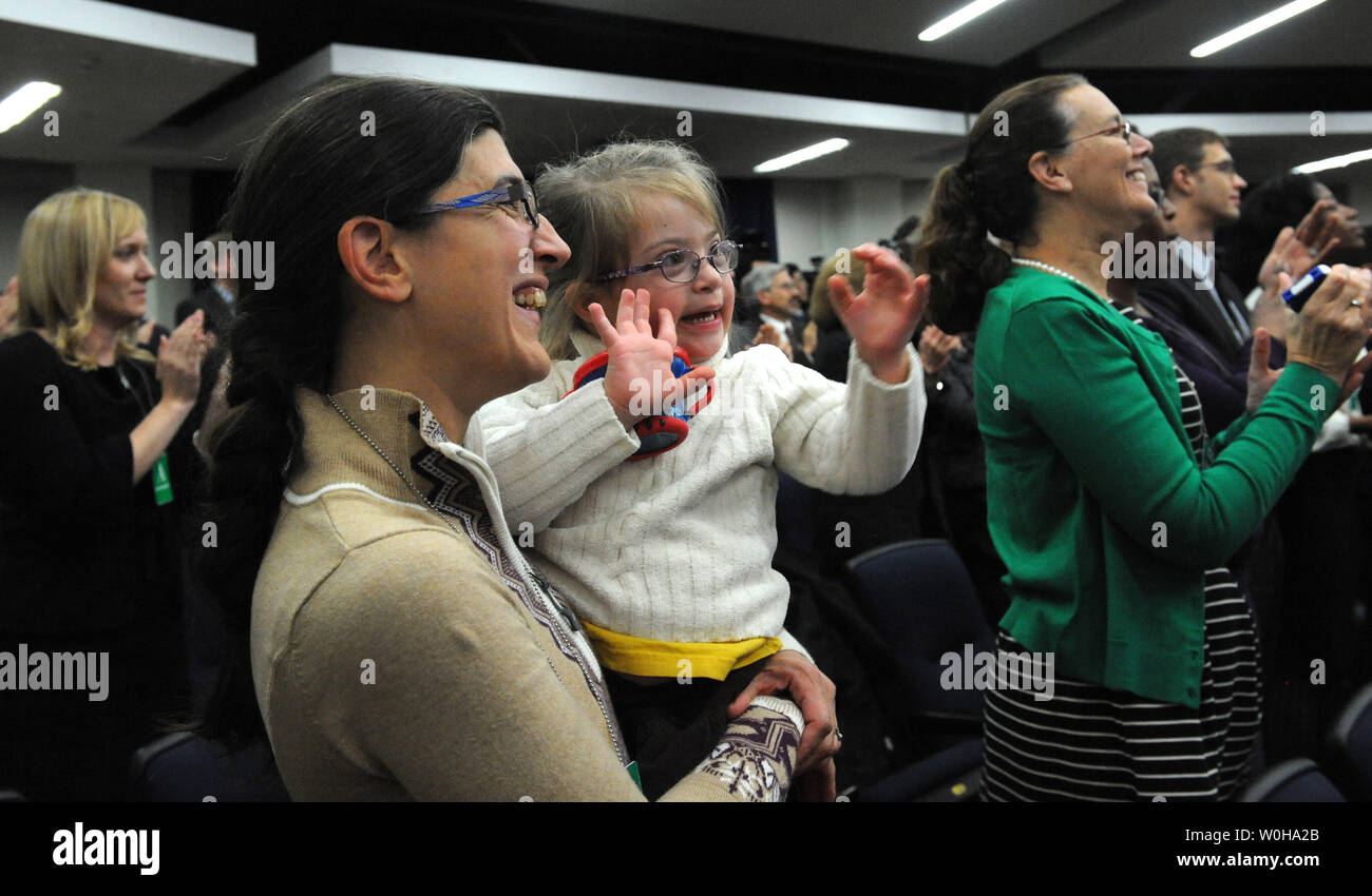 Hope Katz-Zogby, age 3, applauds with her mother Elizabeth as they listen to U.S. President Barack Obama discuss the successes of the Affordable Care Act in the Eisenhower Executive Office Building in Washington, DC on December 3, 2013.   Hope, from Baltimore, Maryland, has Down Syndrome but is guaranteed health insurance under the ACA, since insurance companies cannot bar anyone with pre-existing medical conditions. Obama promised that his signature healthcare law was going to remain as long as he was president and that the troubled www.healthcare.gov website was working well for the vast maj Stock Photo
