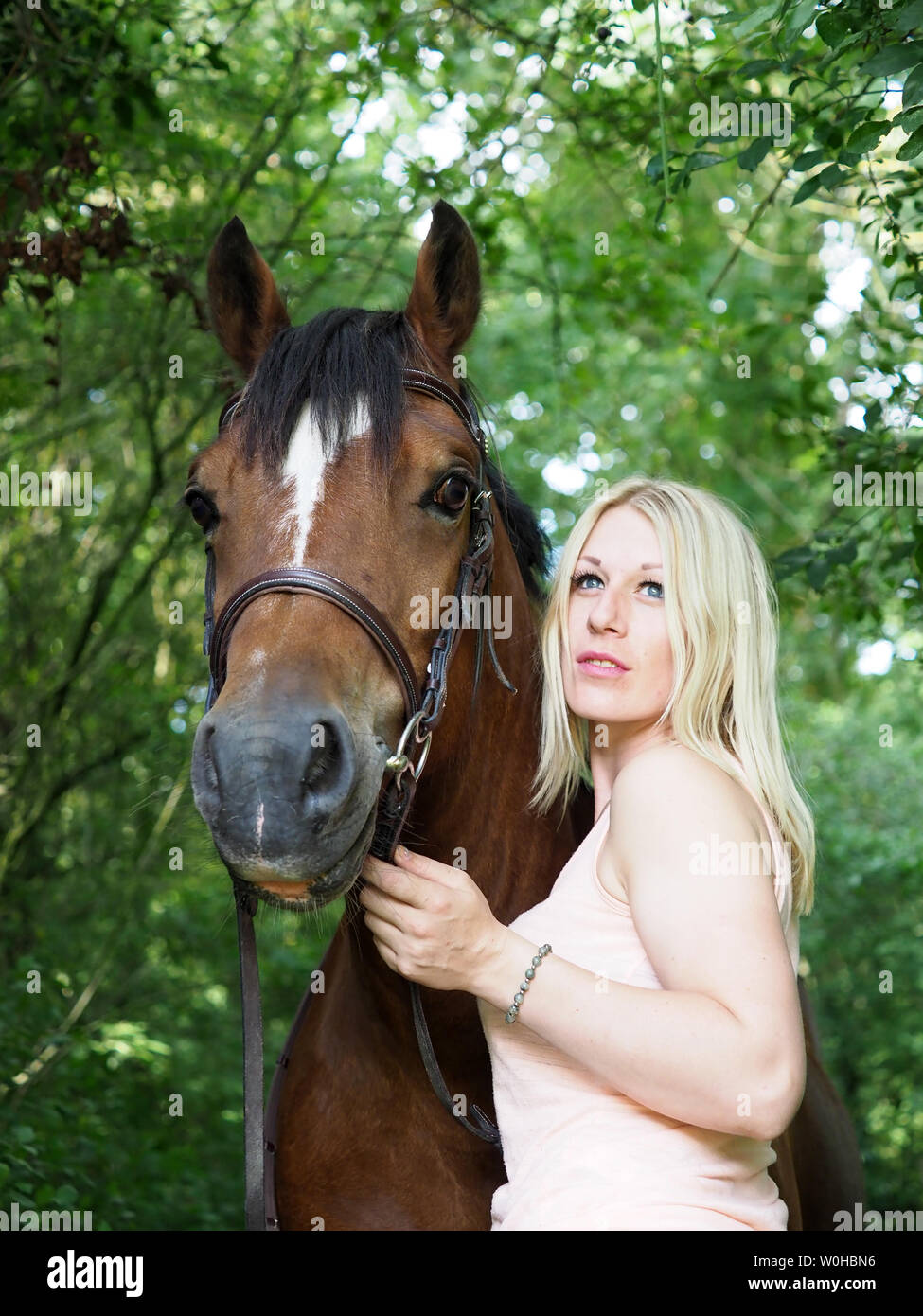 A pretty young blonde woman stands next to her bay Welsh pony. Stock Photo