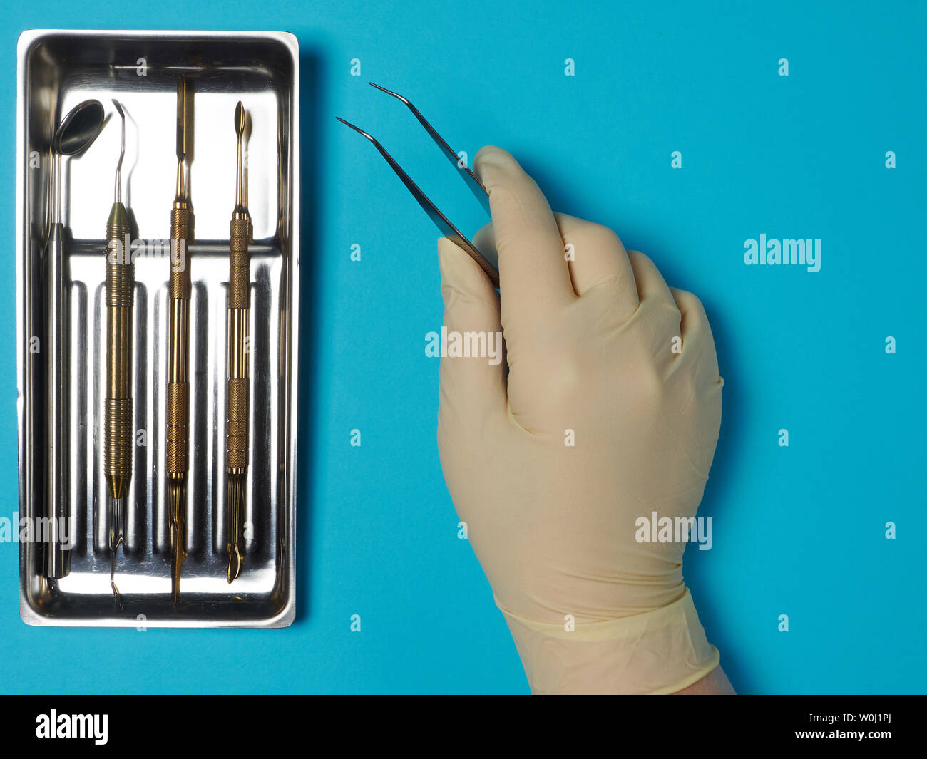 Dental instruments in tray and dentist hand on blue background Stock