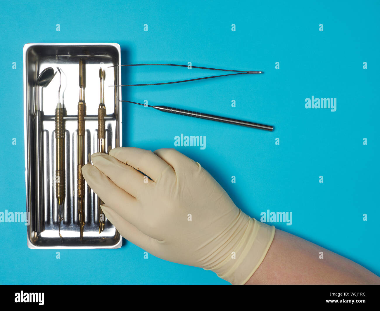 Dental instruments in tray and dentist hand on blue background Stock