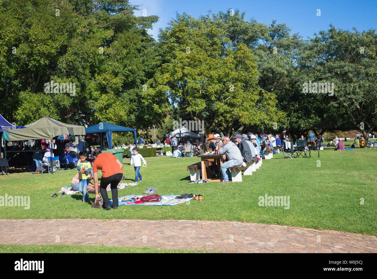 people, tourists, locals sitting in Autumn or Fall sunshine outdoors at tables and benches at a market at Blaauwklippen wine estate in Stellenbosch Stock Photo
