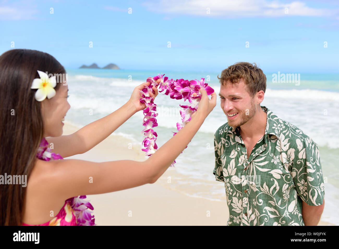 Hawaii woman giving lei garland of pink orchids welcoming tourist on Hawaiian beach. Portrait of a Polynesian culture tradition of giving a flower necklace to a guest as a welcome gesture. Stock Photo