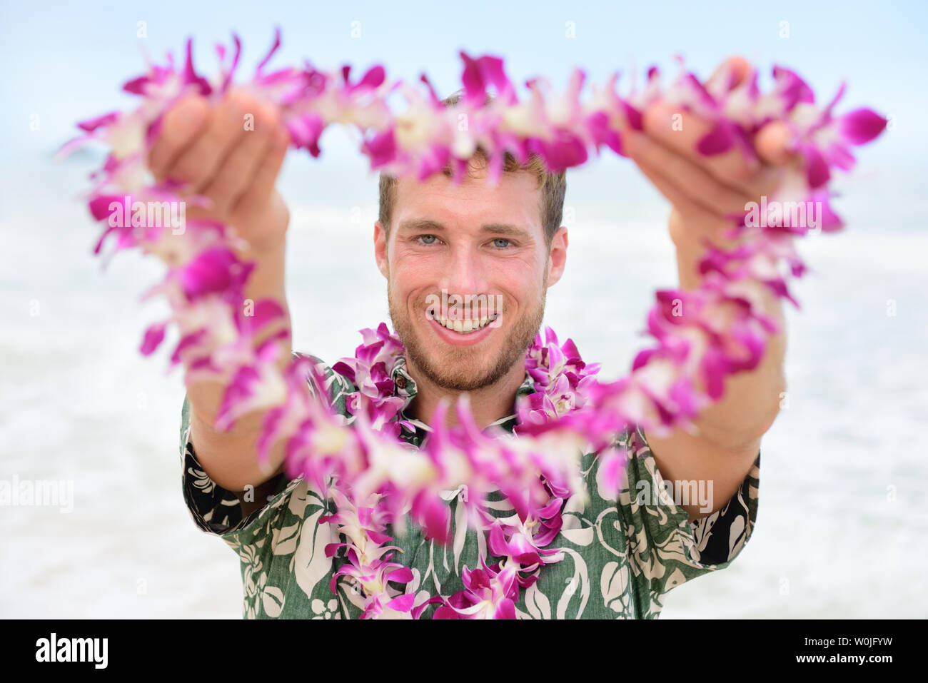 Hawaii Caucasian man with welcome Hawaiian lei. Male tourist portrait holding flower necklace giving it to the camera as a welcoming gesture for tourism in Hawaii. Travel vacation concept. Stock Photo