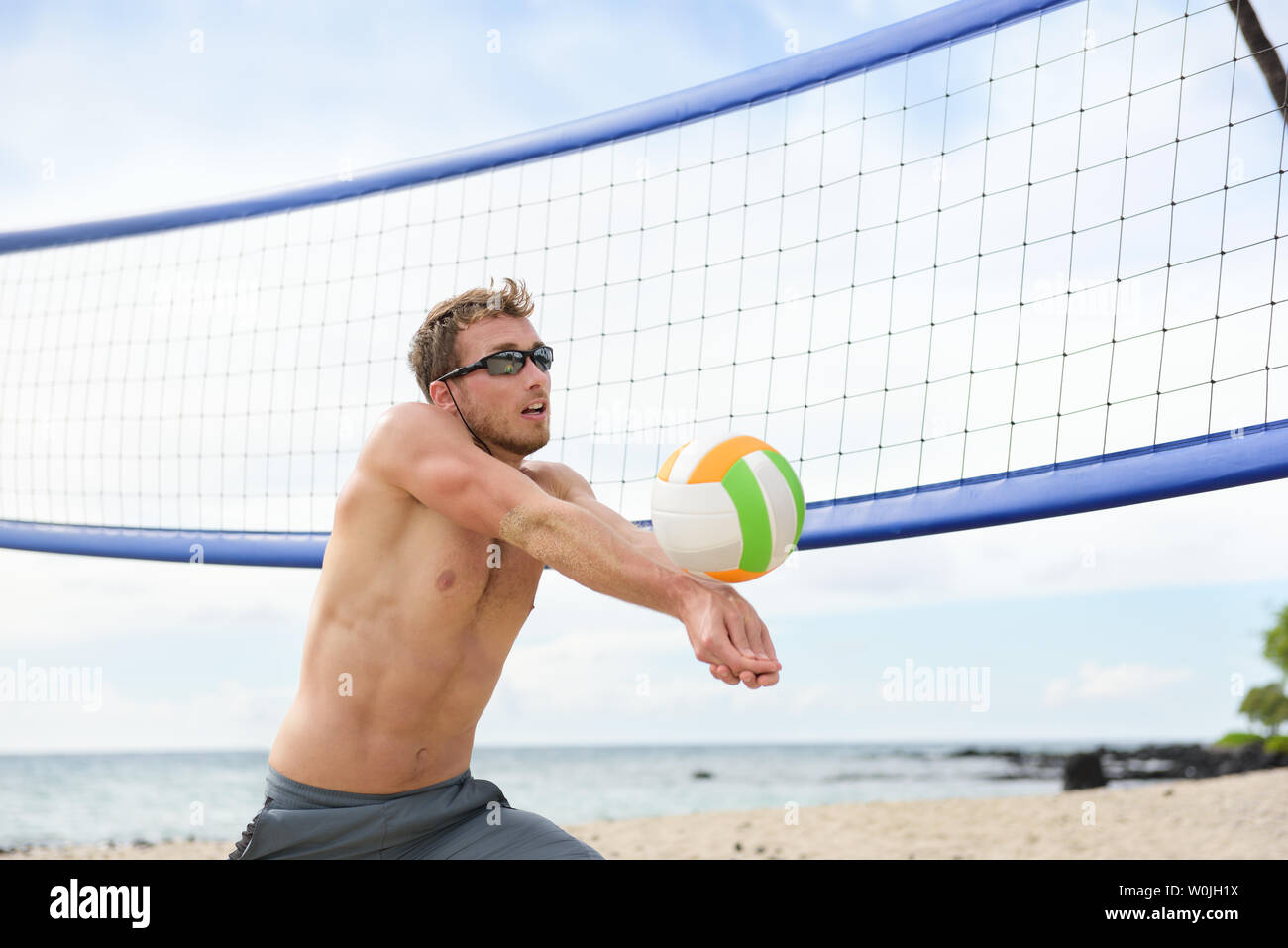 Beach volleyball man playing game hitting forearm pass volley ball during match on summer beach. Male model living healthy active lifestyle doing sport on beach. Stock Photo