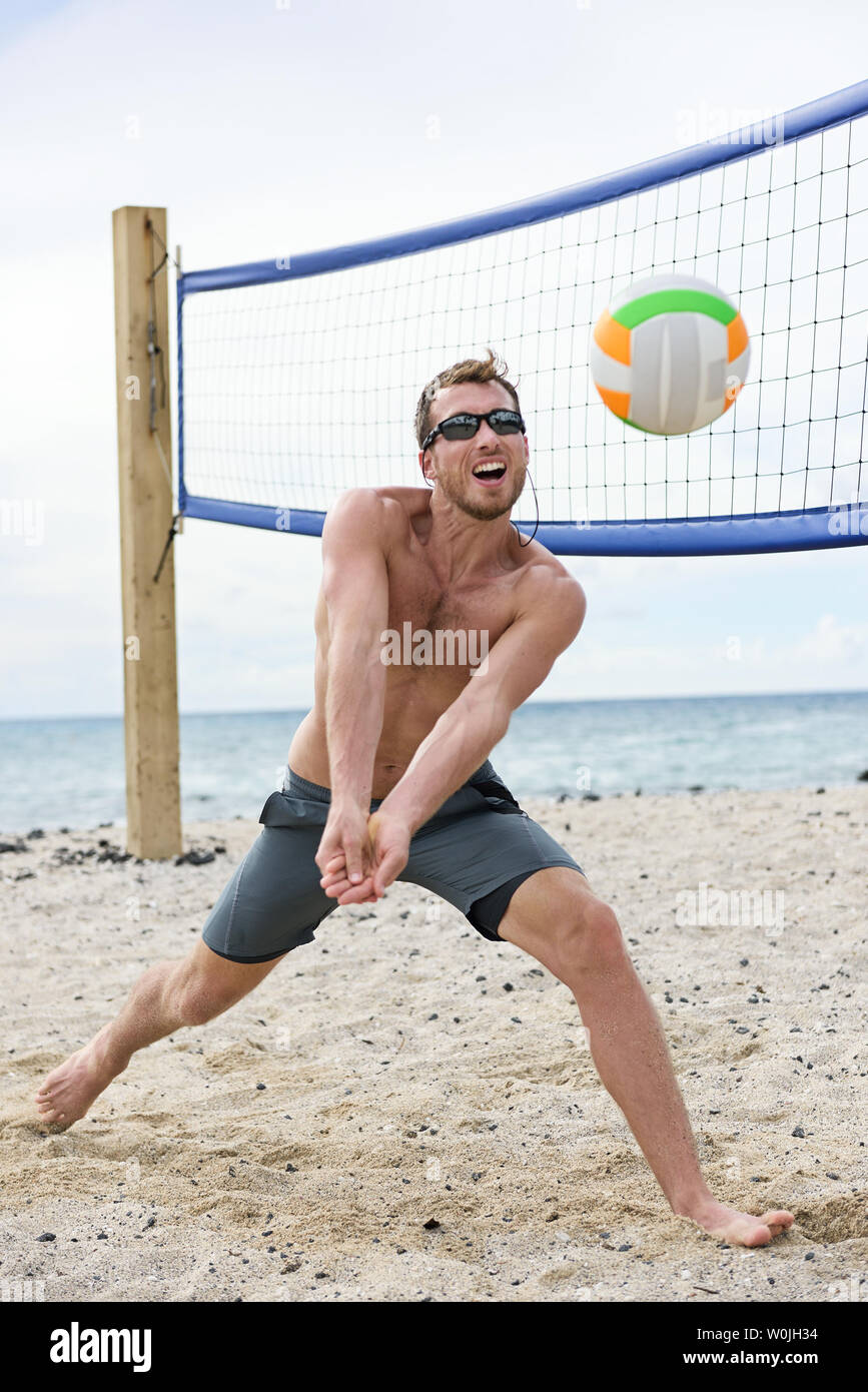 Man playing beach volleyball game hitting forearm pass volley ball on summer beach. Male model living healthy active lifestyle doing sport on beach wearing sunglasses Stock Photo