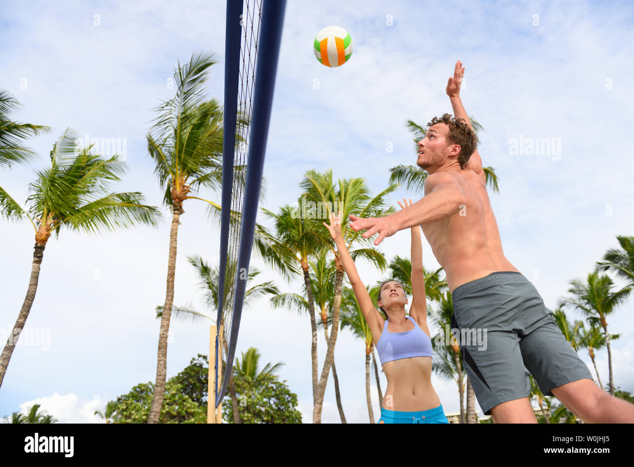 Friends playing beach volleyball sport in summer. Woman volley the ball