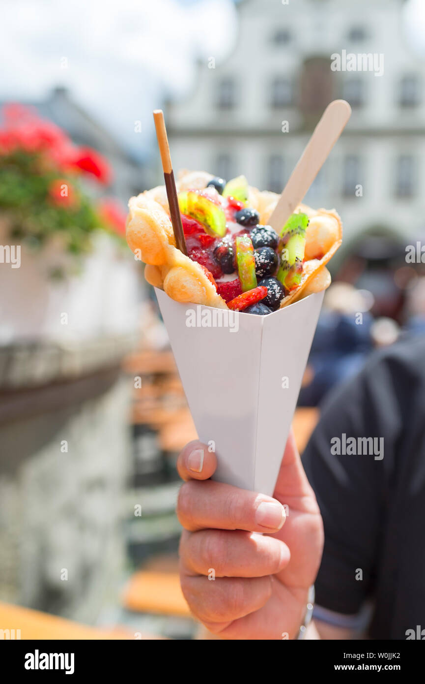 In historic old town (Brilon, Germany) is Cheat Day. A man holds up a paper bag with bubble waffles with fruit. The bag provides space for your own cr Stock Photo