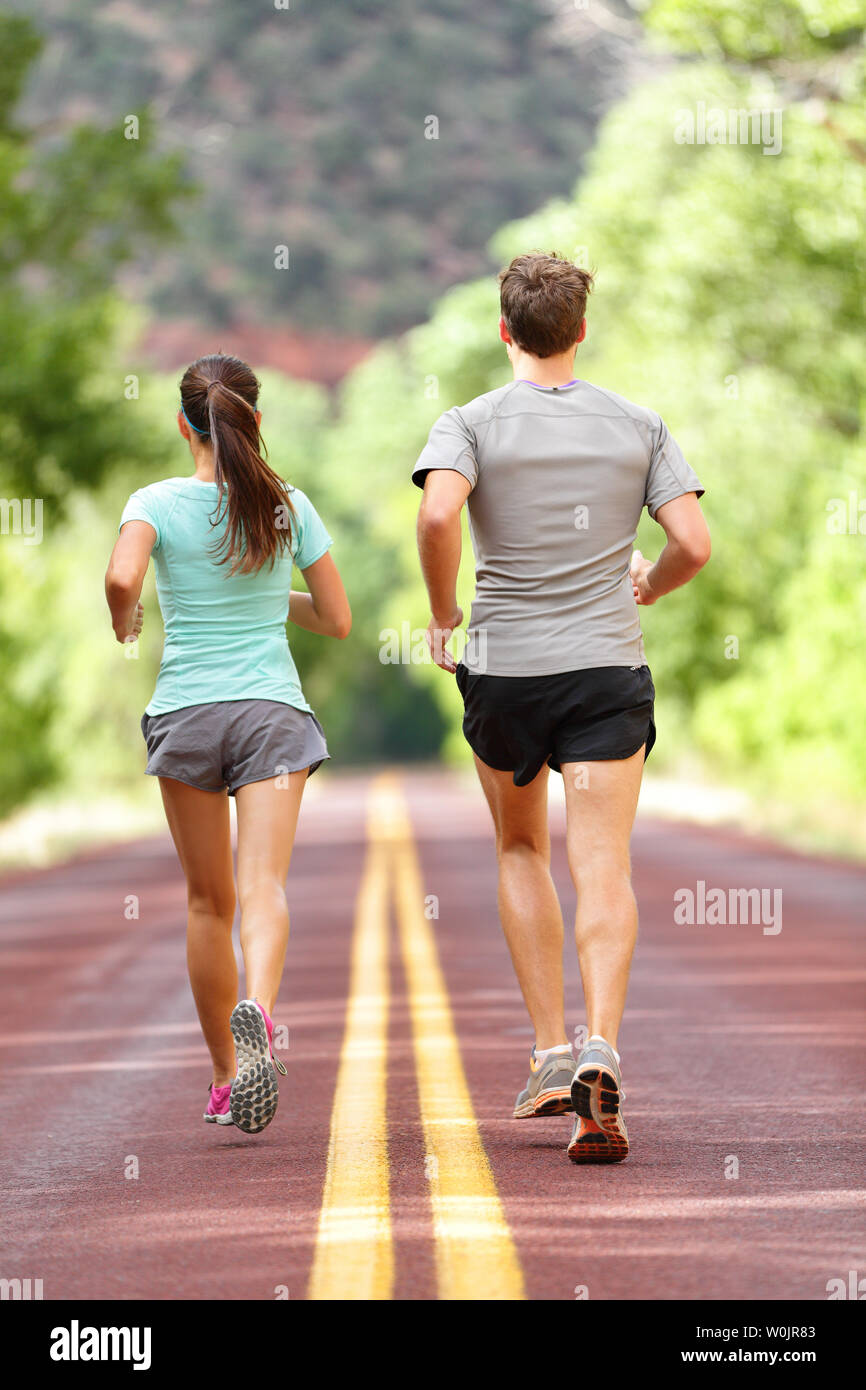 Runners running and jogging for health and fitness. People on fitness run on road in nature. Couple, woman and man training outside for fitness and healthy life. Full body length rear view of back. Stock Photo