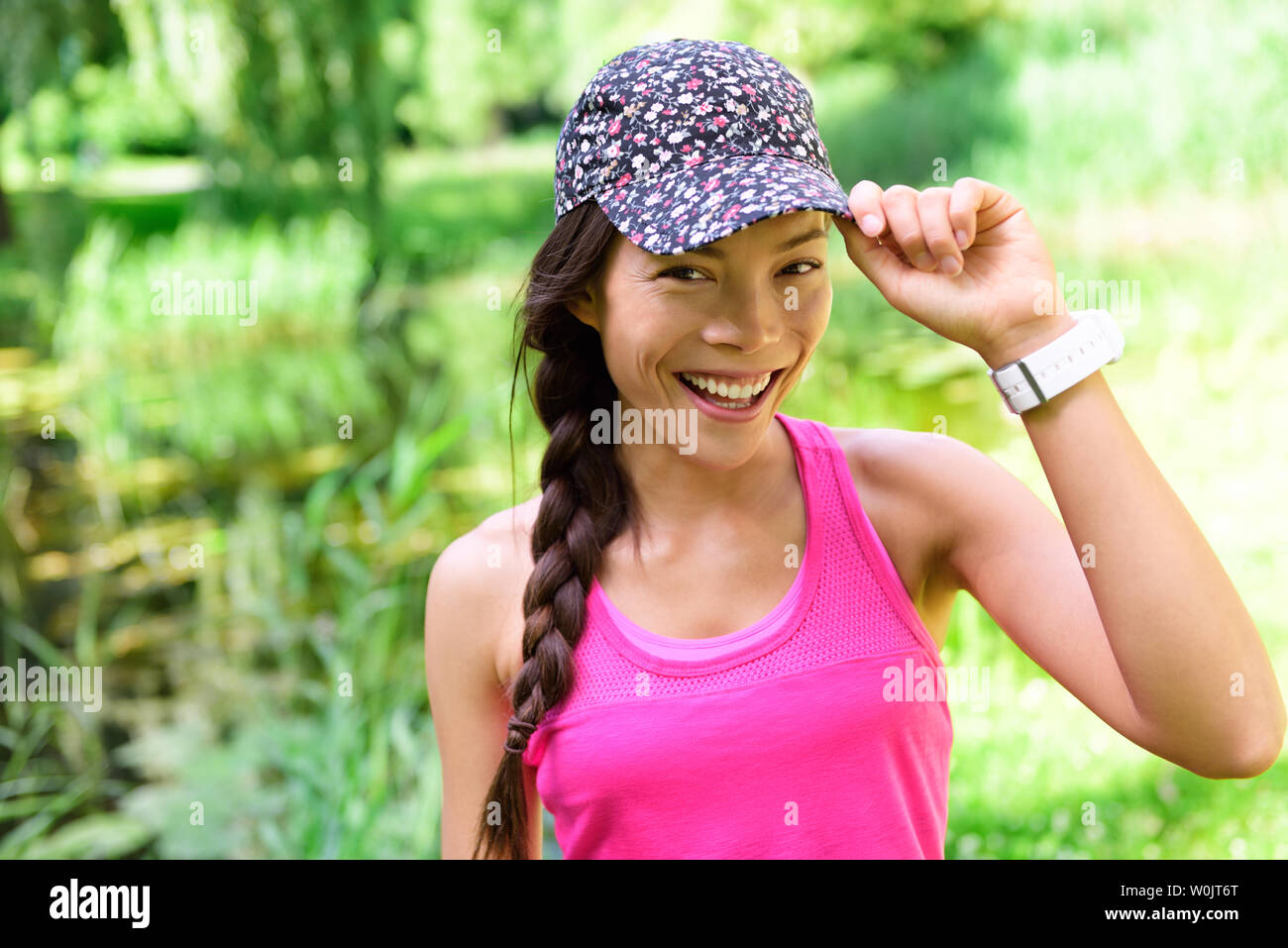 Portrait of woman runner wearing running cap. Female athlete smiling happy at camera after jogging in city park wearing floral headwear hat. Stock Photo