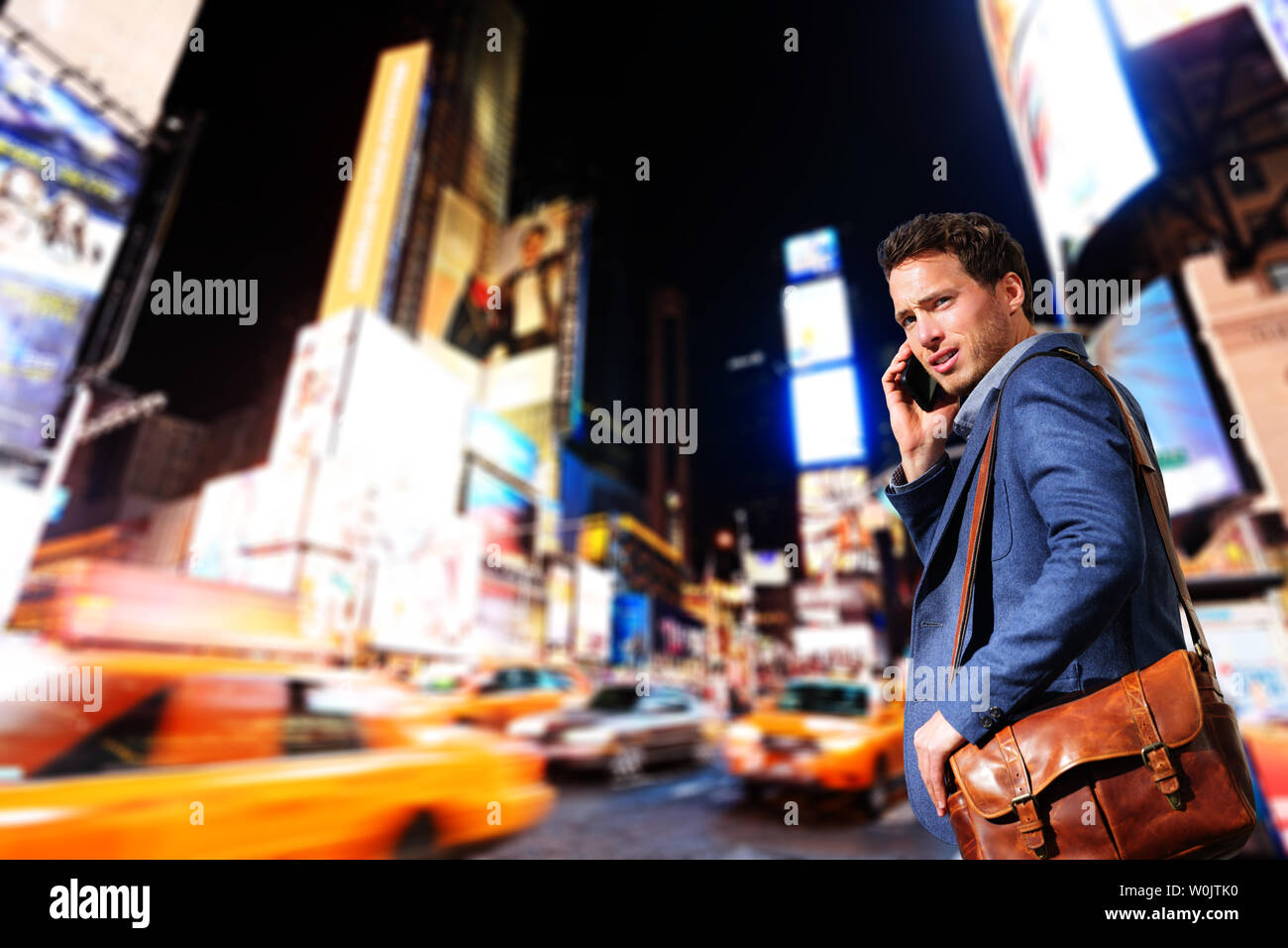 Young urban professional business man talking on smart phone onTimes Square, Manhattan, New York City. Young hip male businessman in casual suit in at night outdoors. Stock Photo