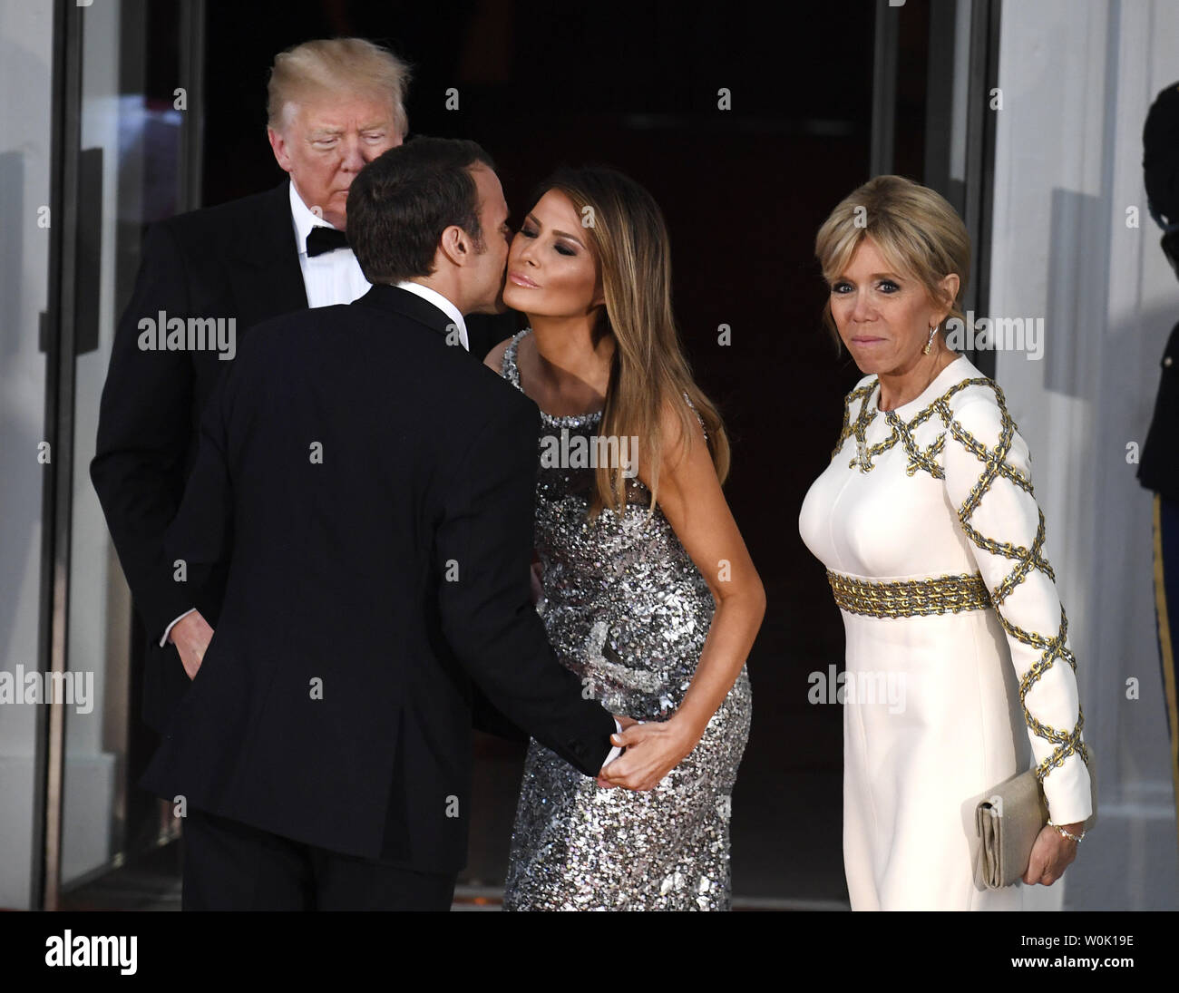 President Donald Trump (L) stands by as French President Emmanuel Macron  greets First Lady Melania Trump with a kiss as he and his wife Brigitte  arrive for a State Dinner at the