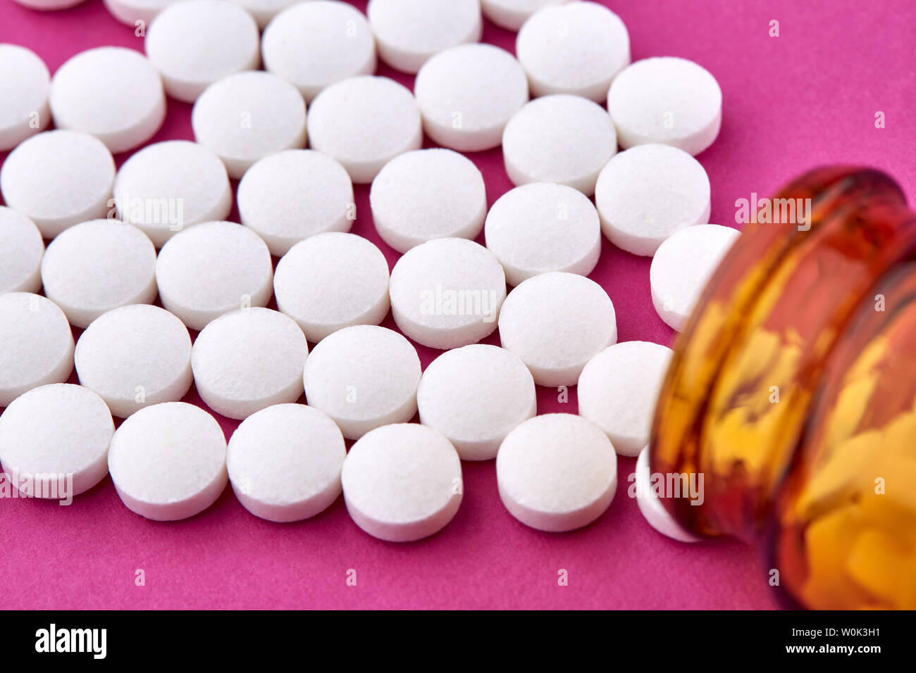 Many white pills and brown vial on pink background. Stock Photo