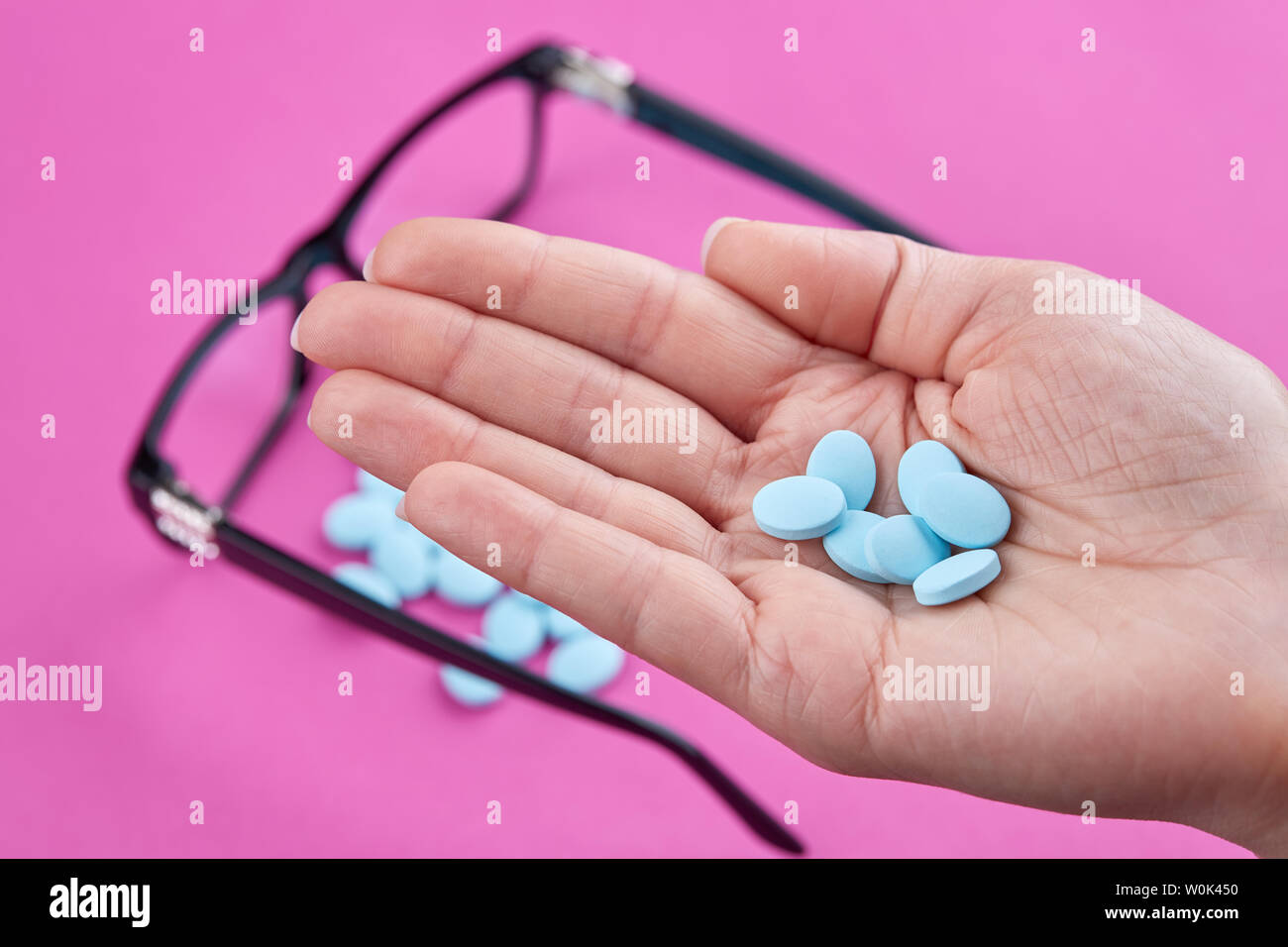 Blue pills in hand and glasses on pink background. Stock Photo