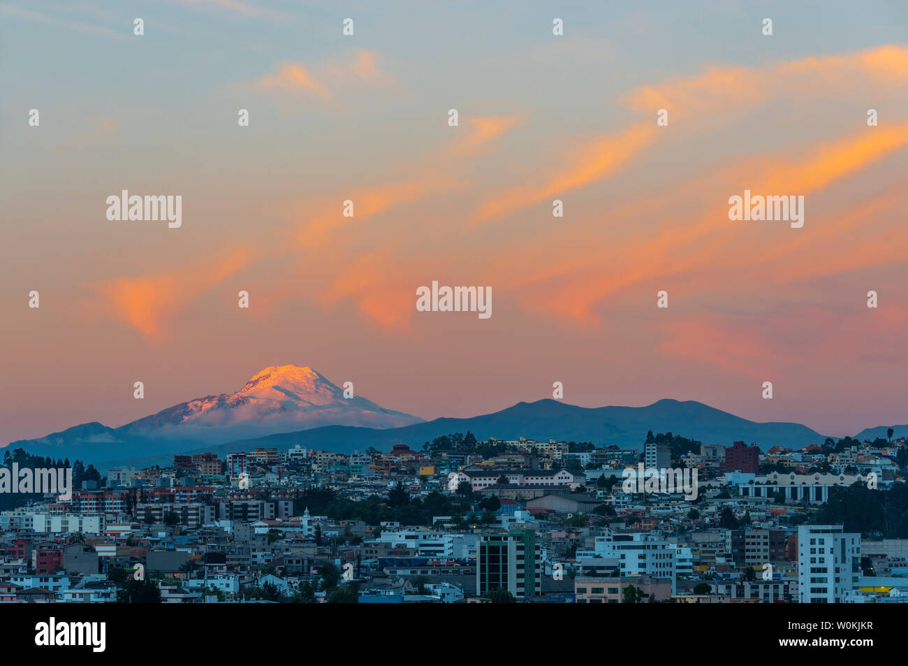 The majestic snowcapped Andes peak of the Cayambe volcano illuminated at sunset with the cityscape of Quito, Ecuador. Stock Photo