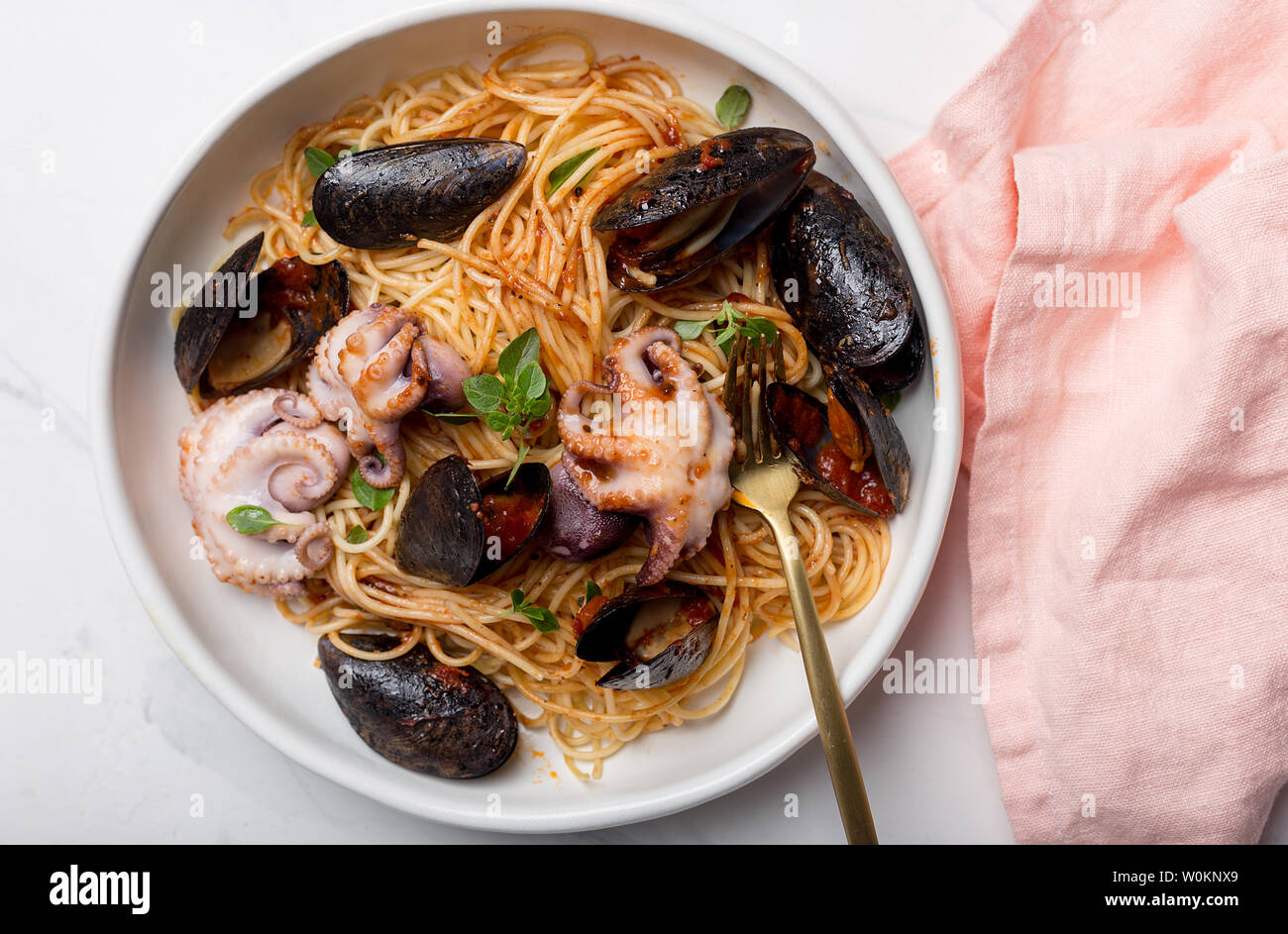 Pasta with seafood and tomato sauce. Spaghetti with octopus and mussels in white bowl with fork and pink napkin on white background. Concept of seafoo Stock Photo