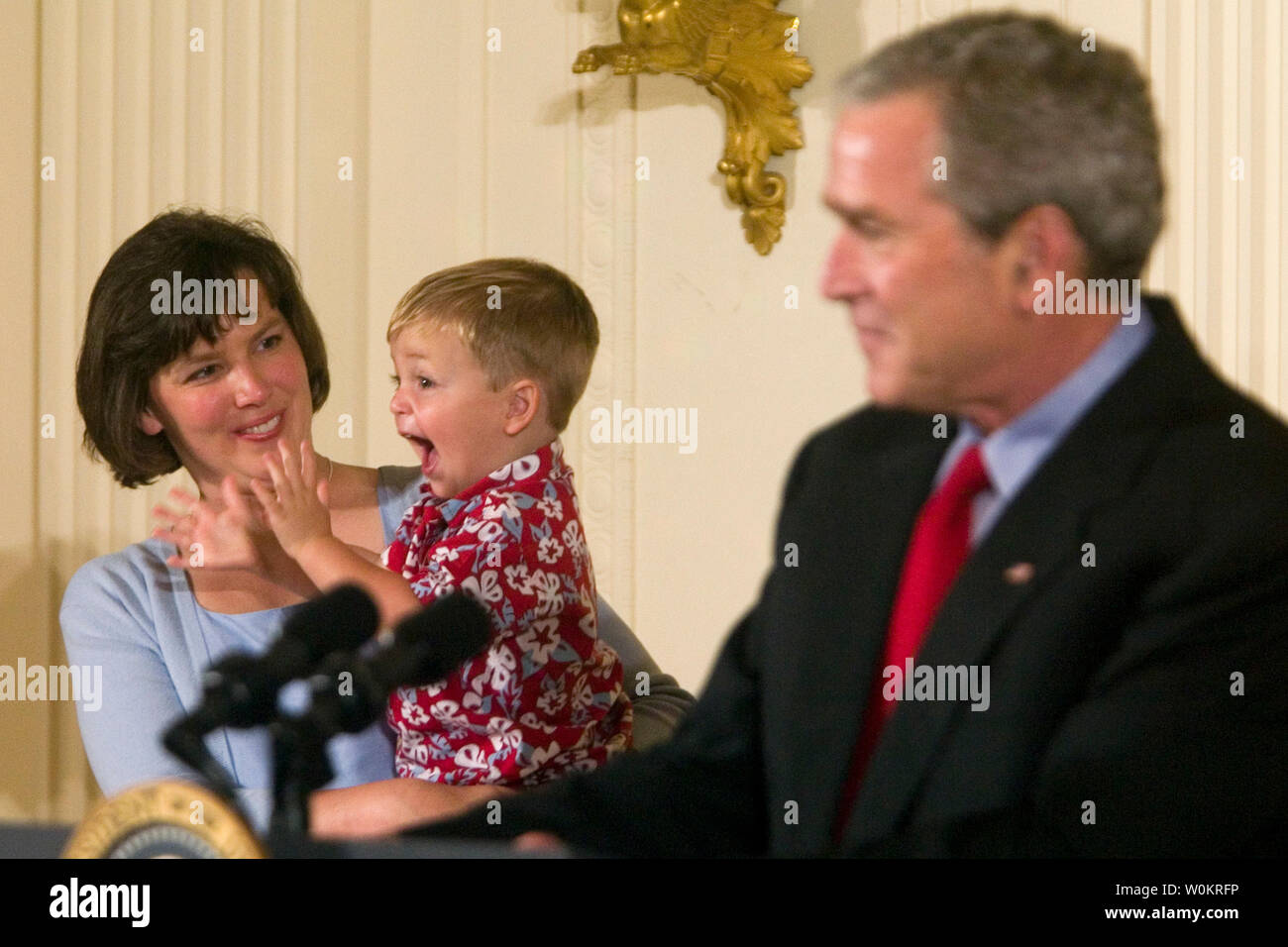 Courtney Atnip, left, holds her son Carter as President George W. Bush delivers a speech on bioethics in the East Room of the White House in Washington, mAY 24, 2005.  Twenty-one families adopted children from embryos appeared as guests. The White House is criticizing pending legislation that would loosen restrictions on government funding of embryonic stem cell research as a vote in the U.S. House of Representatives draws near. (UPI Photo/Kamenko Pajic) Stock Photo
