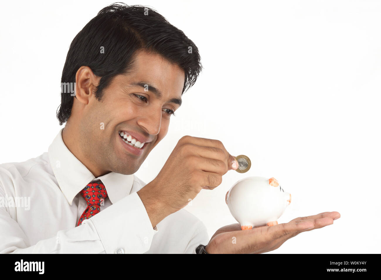 Indian businessman inserting a coin into a piggy bank Stock Photo