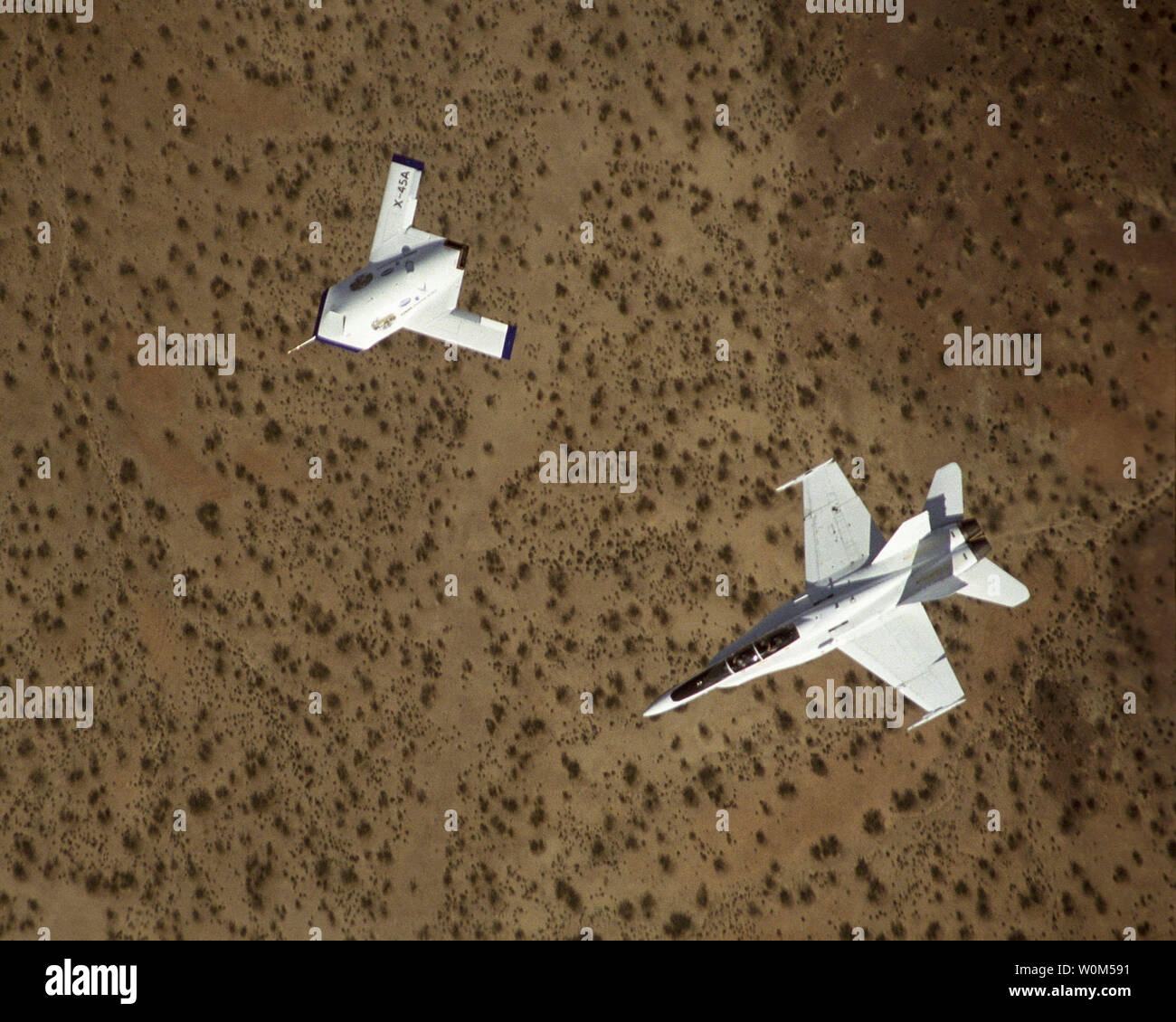 An F-18 flies chase for a Joint Unmanned Combat Air Systems X-45A during a test drop of a GPS-guided munition over China Lake Warfare Center Weapons Division Range, China Lake near Ridgecrest, Calif., recently.   (UPI Photo/NASA Chase) Stock Photo