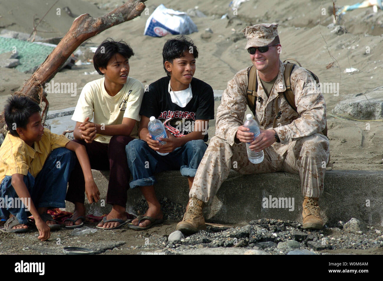 Marine Capt. Jamey Stover, assigned to the 15th Marine Expeditionary Unit (MEU), sits down with local Indonesian children as Sailors and Marines offload supplies from a Landing Craft Air Cushion (LCAC) in Meulaboh, Sumatra, Indonesia on Jan. 11, 2005.   (UPI Photo/Alan D. Monyelle/US Navy) Stock Photo