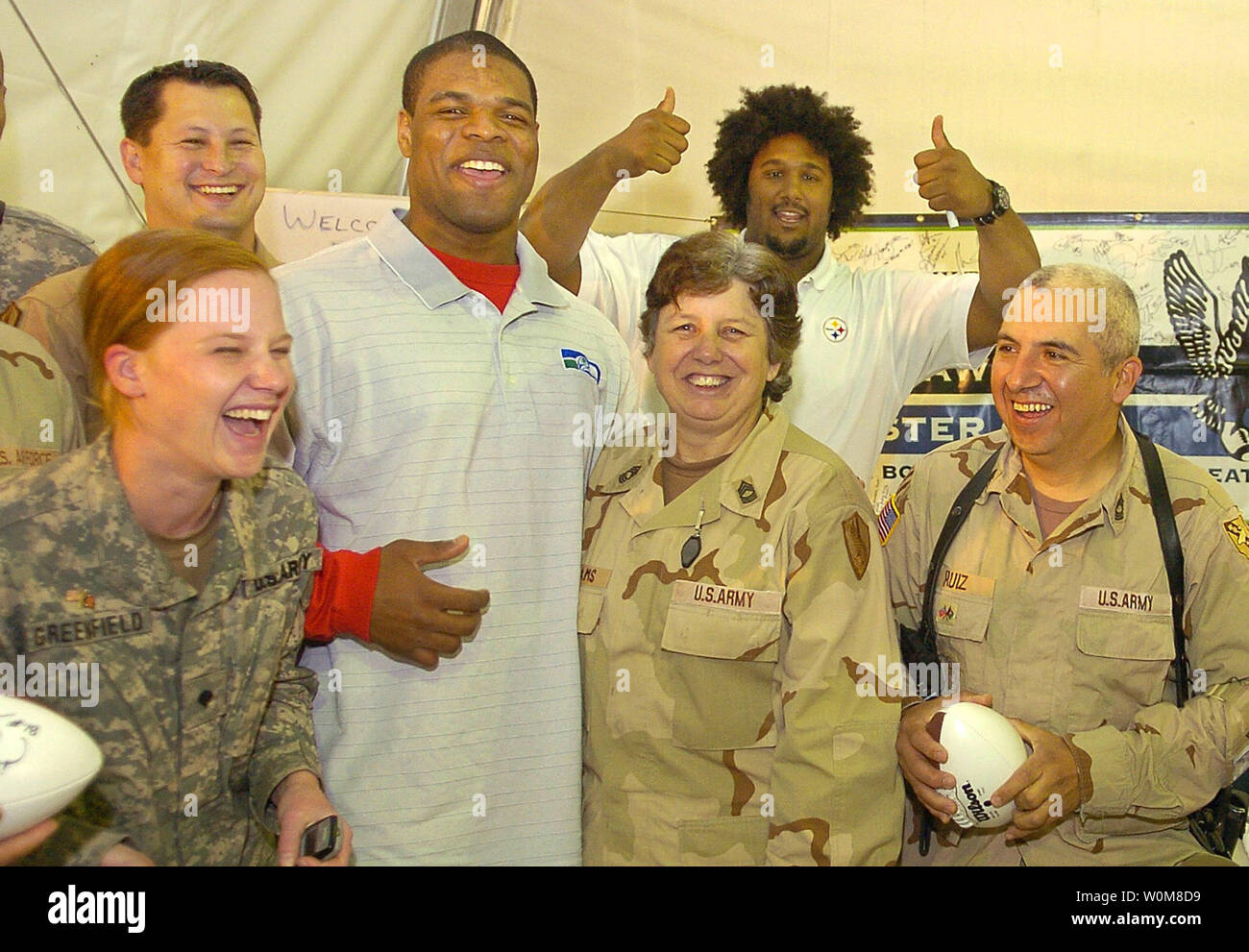 Pittsburgh Steelers Max Starks (background) crashes a group photo of Seattle Seahawks Bryce Fisher and military Seahawks fans during a USO visit to Camp Eggers in Kabul, Afghanistan on April 4, 2006.  Fisher was joined by MSgt. Traci Williams (C), who is the Seahawks' Military Liason and is now deployed in Afghanistan. US troops Spc. Jessica Greenfield (L), Evansville, IN and MSgt. Jesus Ruiz (R), San Antonio, TX joined in. The USO and NFL are marking a 40-year relationship of supporting US military with morale-boosting visits around the world.   (UPI Photo/Mike Theiler/USO) Stock Photo