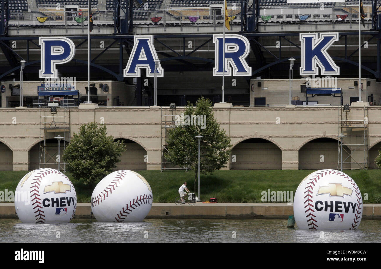 A bicyclist rides past gigantic baseballs floating in the Allegheny River in front of PNC Park