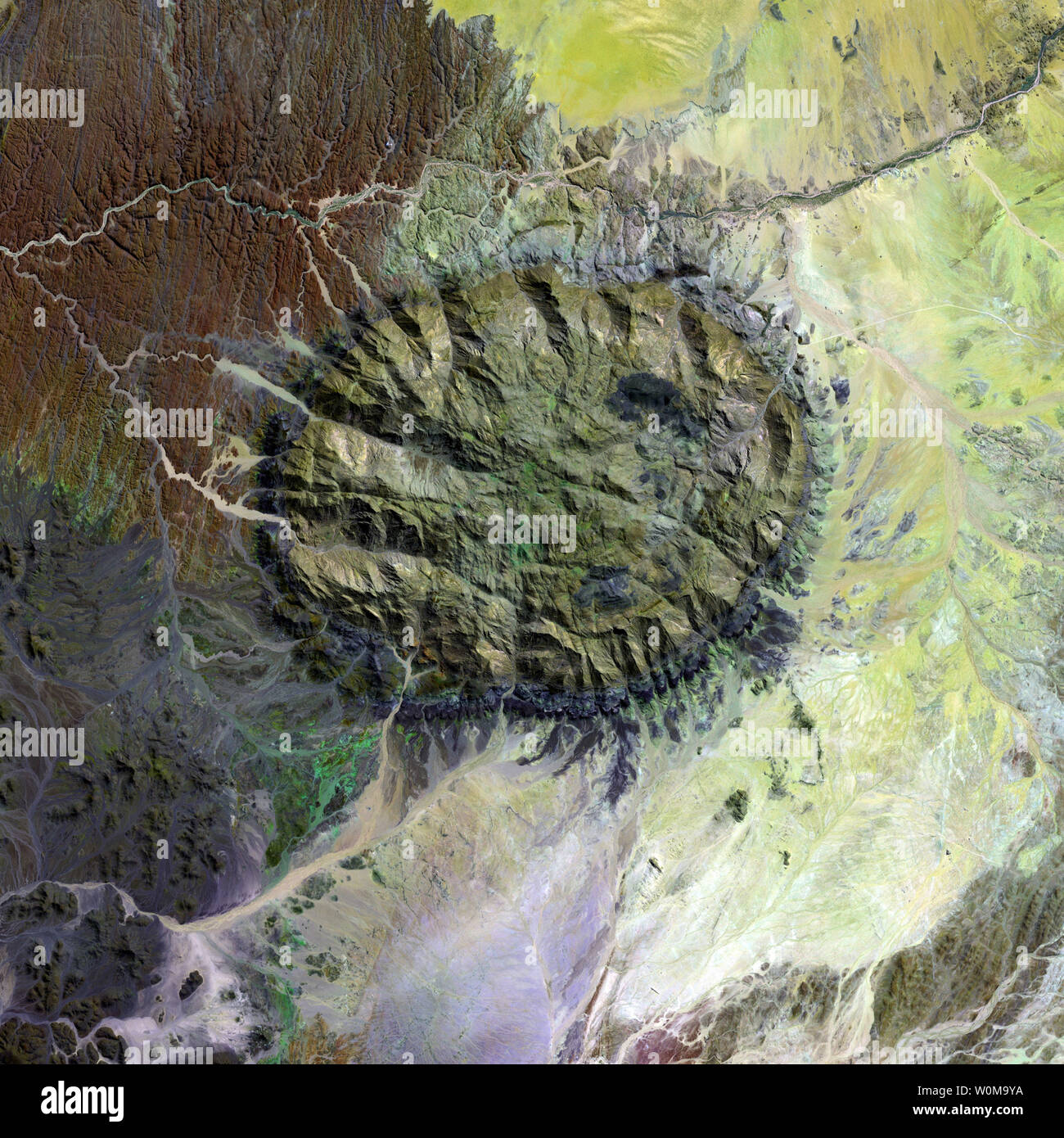 A single mass of granite, clearly visible in this NASA photograph, punched through the Earth's crust over 120 million years ago to create a mountain in northern Namibia near the heart of the Namib Desert. The mountain, called ' Daures', or the 'burning mountain' by Namibians, rises high above the arid desert and a ring of dark, jagged rocks forced up during the mountain's arrival encircles the granite rock. (UPI Photo/NASA) Stock Photo