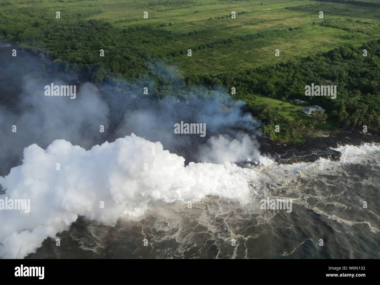 View taken on May 20, 2018, of the lava flow reaching the ocean. Hot lava entering the sea creates a dense white plume called 'laze' (short for 'lava haze'). Laze forms as hot lava boils seawater to dryness. The process leads to a series of chemical reactions that result in the formation of a billowing white cloud composed of a mixture of condensed seawater steam, hydrochloric acid gas, and tiny shards of volcanic glass. This mixture has the stinging and corrosive properties of dilute battery acid. Because laze can be blown downwind, its corrosive effects can extend far beyond the actual ocean Stock Photo