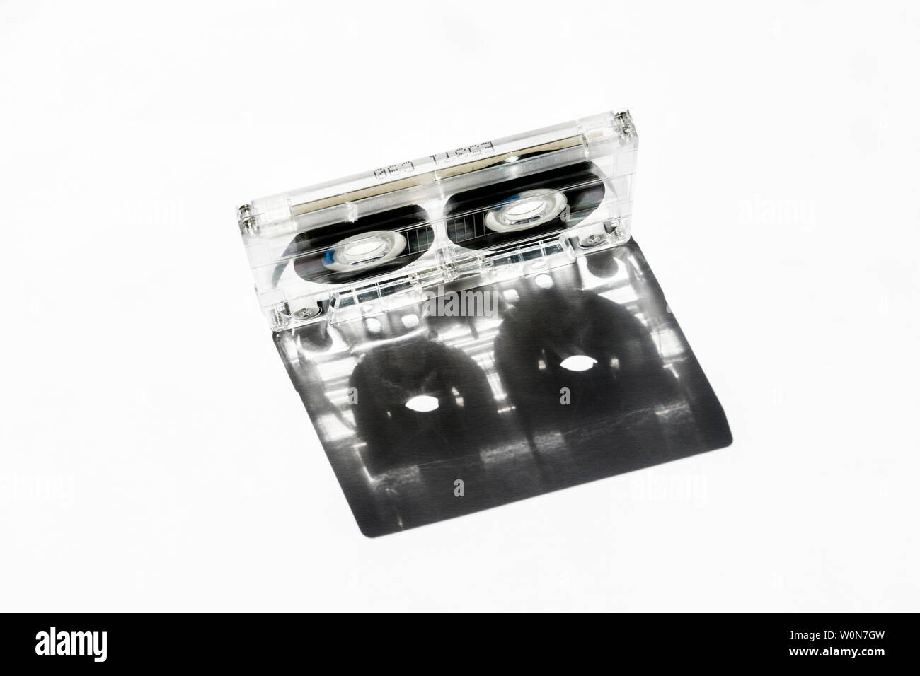 Transparent plastic C90 compact cassette audio tape casting a shadow against a white background Stock Photo