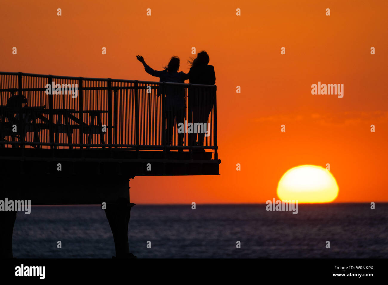 Aberystwyth Wales UK, Thursday   27 June 2019  UK Weather: Two women stand at the end of the seaside pier,  watching the glorious sunset in Aberystwyth on the Cardigan Bay coast, west Wales. The country is heading into a spell of fine weather with a plume of hot air drifting up from the continent, bringin with it the hottest days of the summer so far,  with temperatures expected to reach the high 20’s centigrade   photo credit: Keith Morris//Alamy Live News Stock Photo
