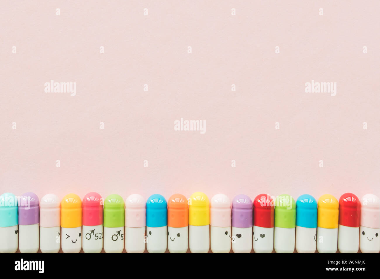 Row of capsule on a pastel paper pink background. Copyspace. Border of Funny multicolored medecines Stock Photo