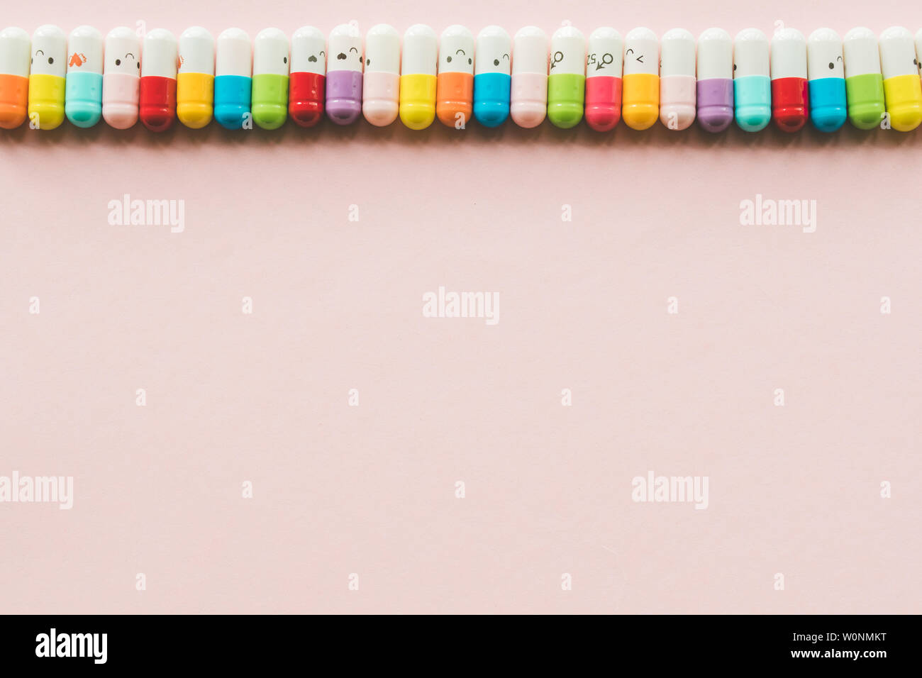 Row of capsule on a pastel paper pink background. Copyspace. Border of Funny colored medecines Stock Photo
