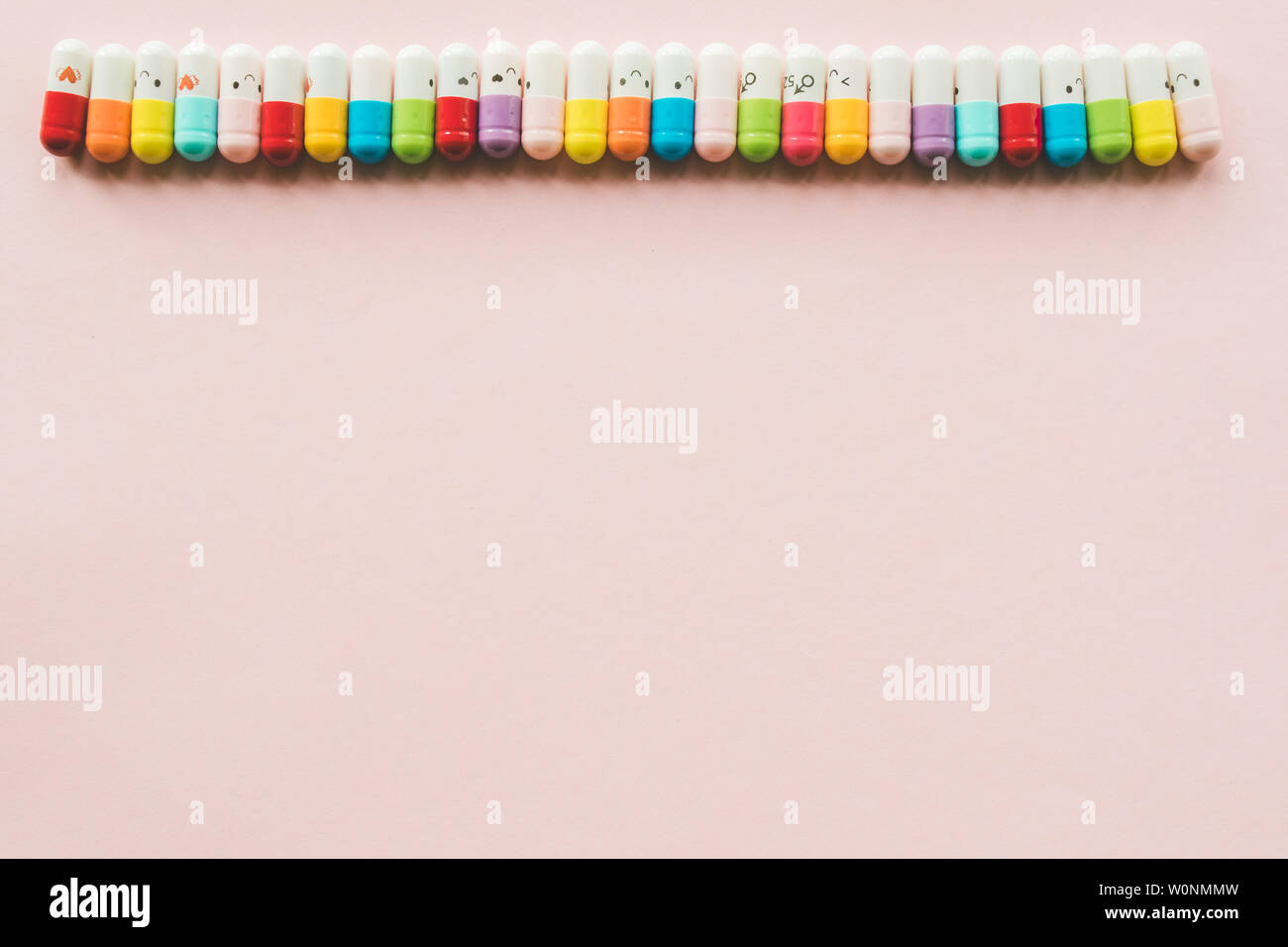 Row of capsule on a pastel paper pink background. Copyspace. Border of Funny multicolored medecines Stock Photo
