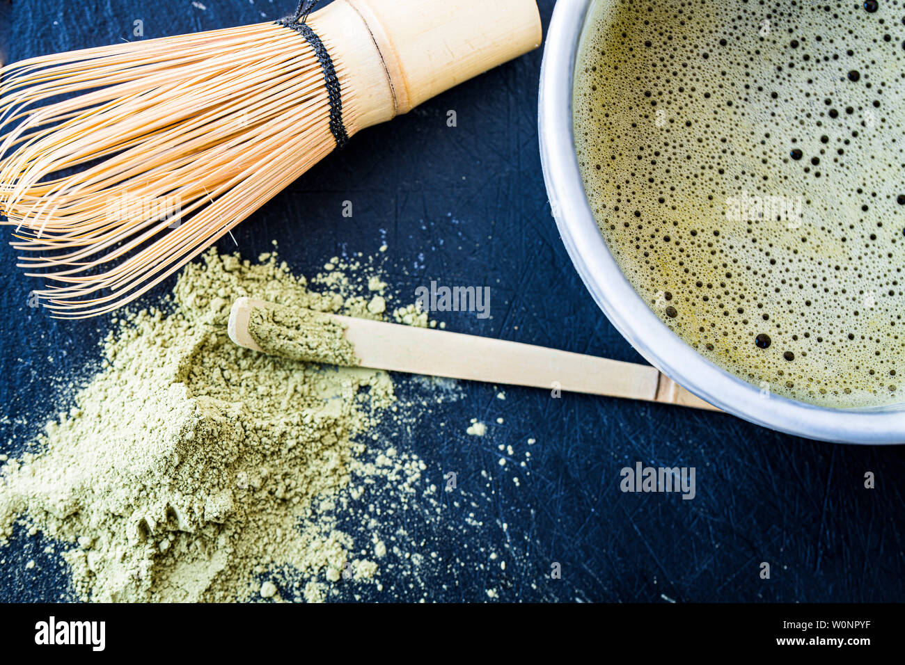 A close up of freshly made matcha green tea in a mug, bamboo whist, bamboo spoon and green tea powder Stock Photo