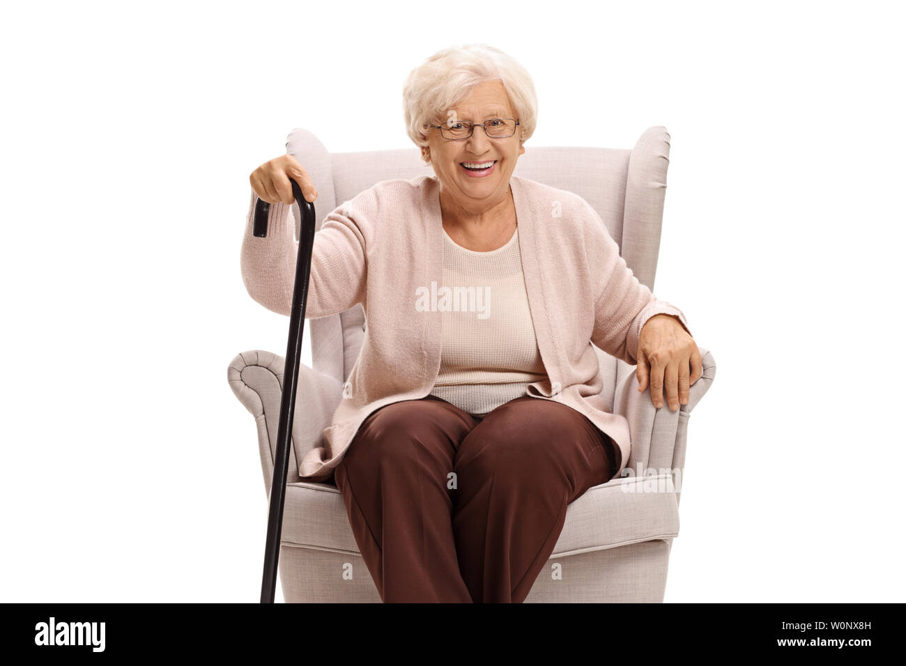 Senior woman with a cane sitting in an armchair and looking at the camera isolated on white background Stock Photo