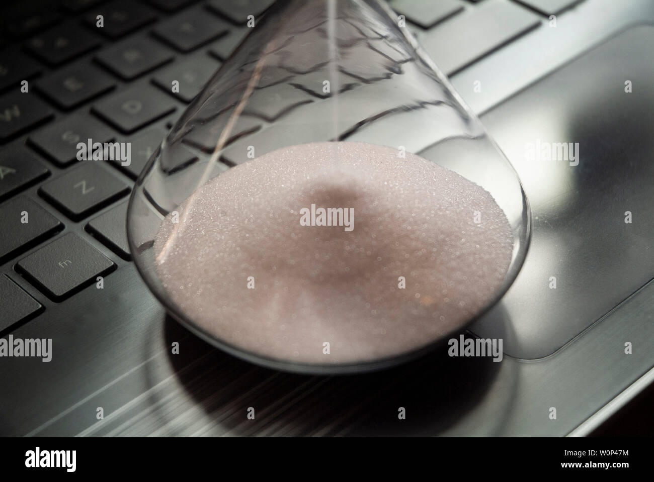 An hourglass sits on a laptop computer. Stock Photo
