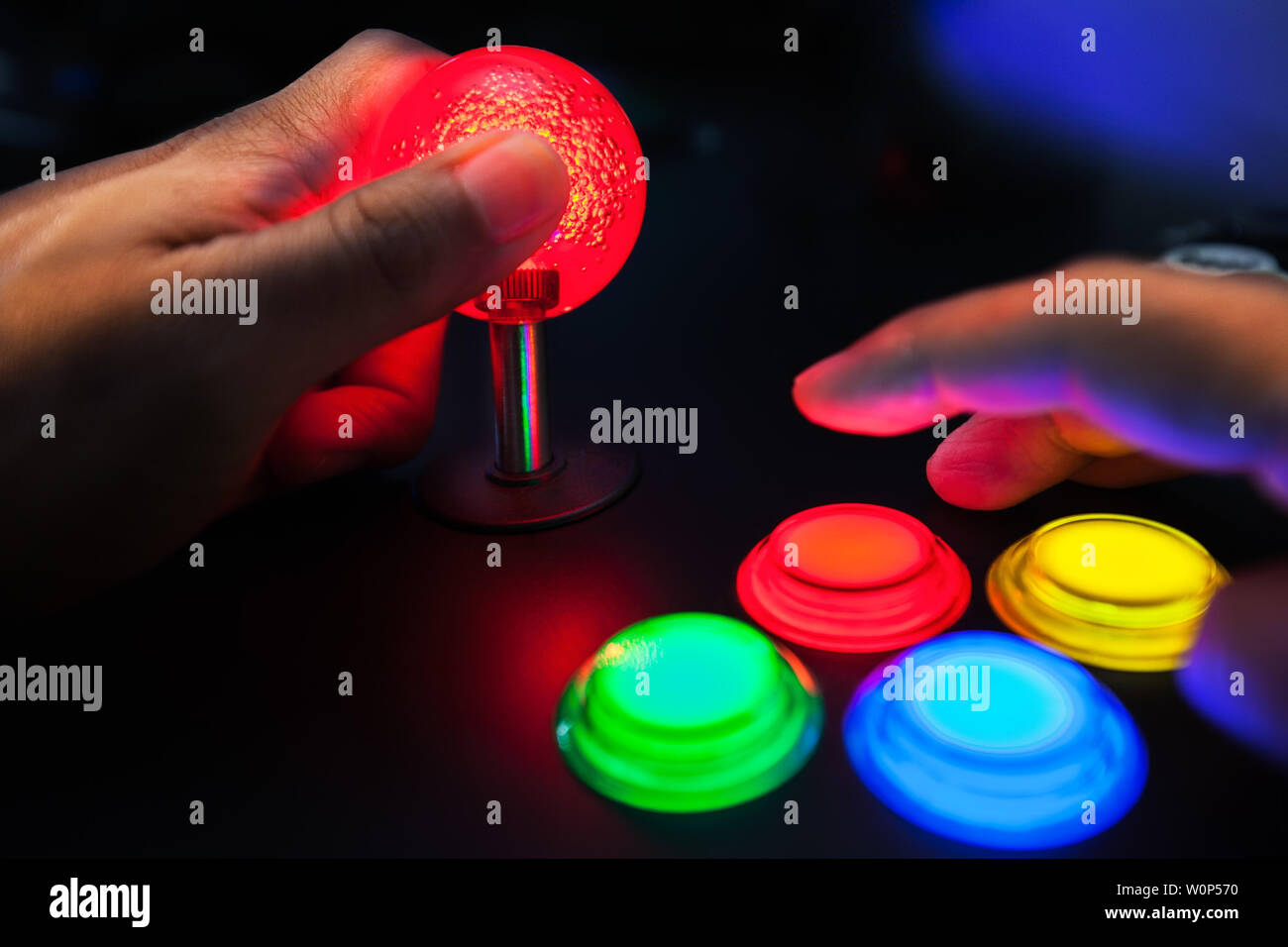 A red lighted arcade joystick and four button layout push buttons being played by a video gamer on a retro arcade machine. Stock Photo