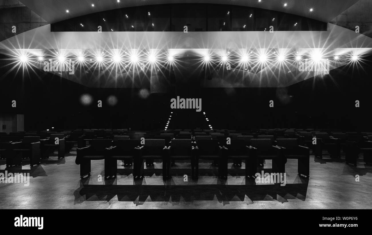 View towards empty audience seats at empty stage in generic acting theater before performance. Strong deliberate spotlights with light flares Stock Photo