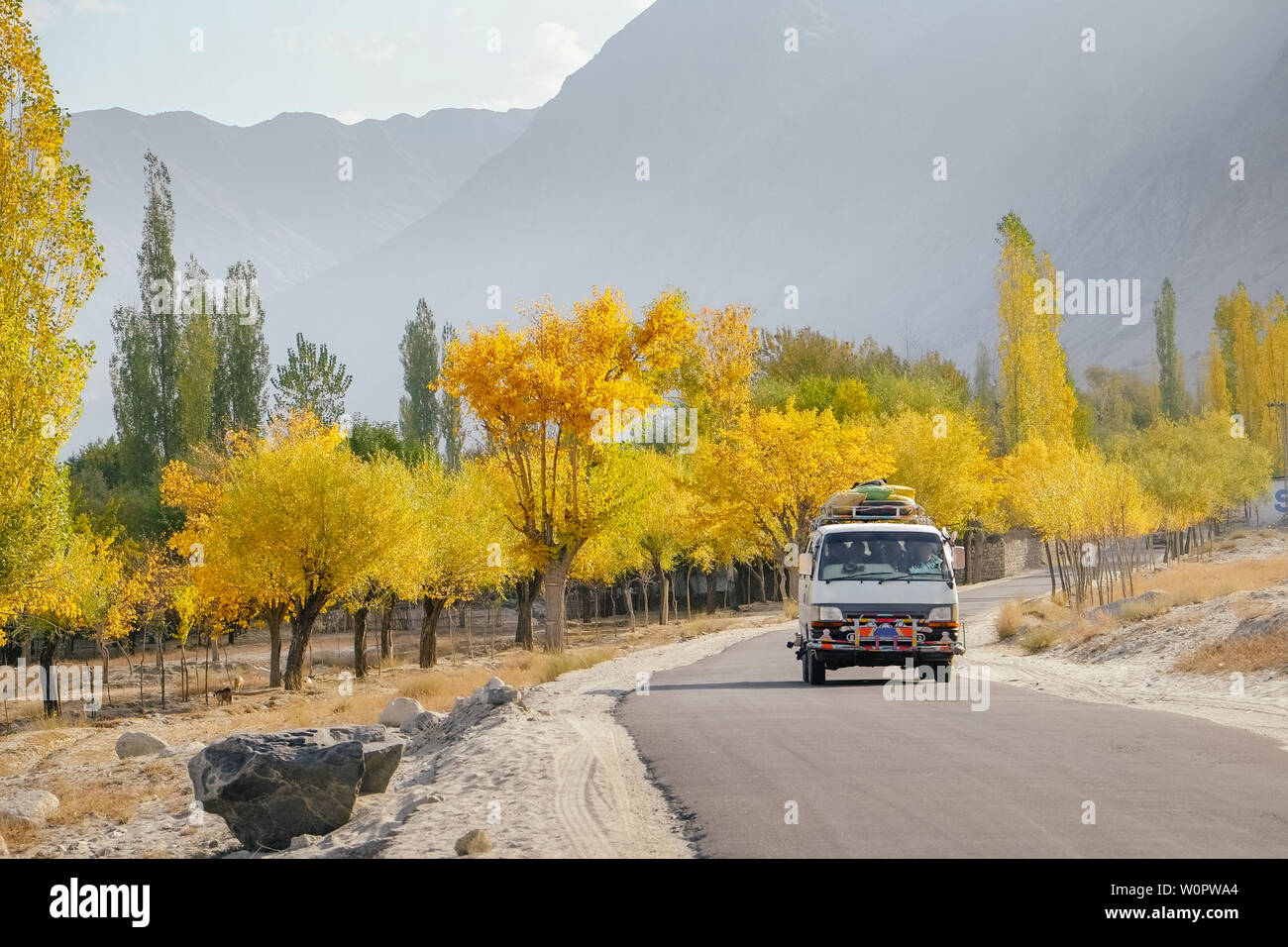 A local bus running on paved road with luggage bags on the roof with landscape view in autumn, Skardu. Gilgit Baltistan, Pakistan. Stock Photo