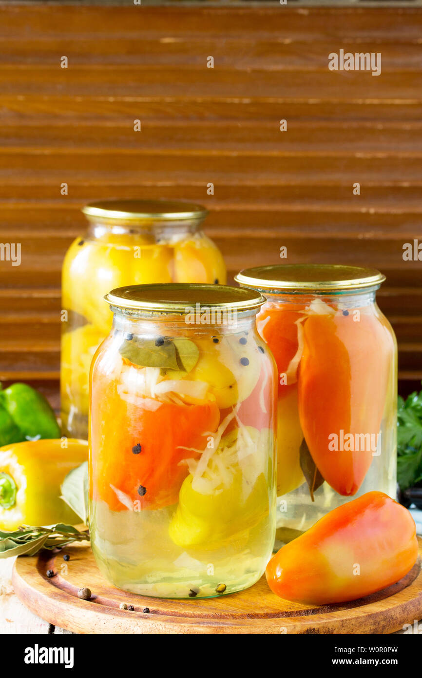 Homemade preserving. Bulgarian Pepper stuffed with vegetables in marinade on the kitchen wooden background. Free space for your text. Stock Photo