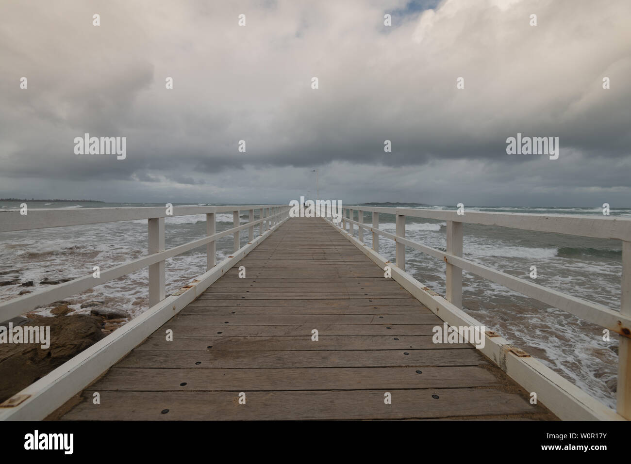 Point Lonsdale pier leads to the horizon with dark storm clouds and angry seas on the Bellarine Peninsula, Victoria, Australia Stock Photo